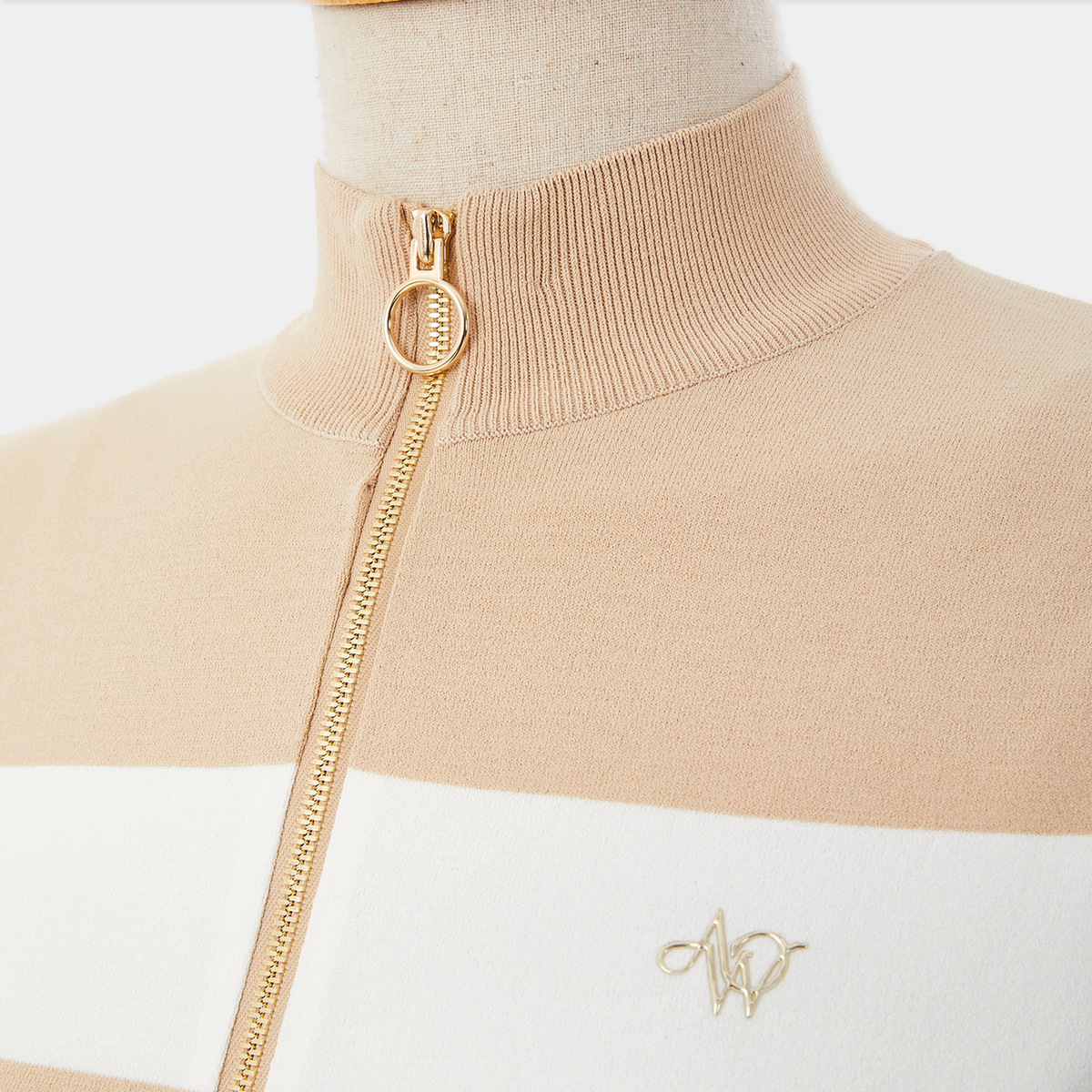 Beige and white sweater with gold zipper on a mannequin against a white background