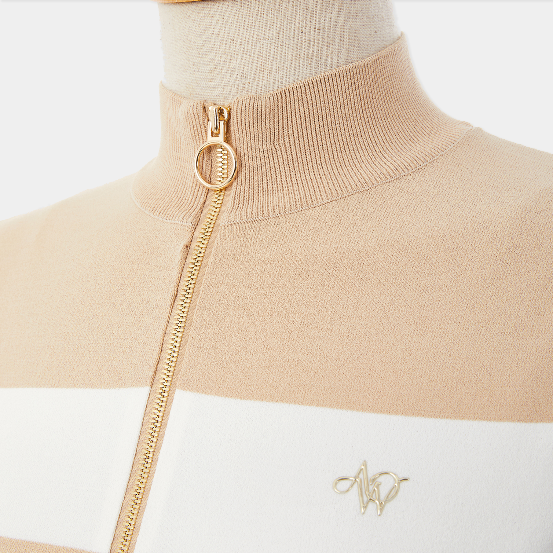 Beige and white sweater with gold zipper on a mannequin against a white background