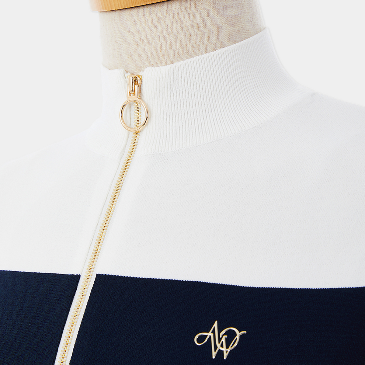 Close-up of a white and navy striped sweater with a gold chain and logo on a mannequin.
