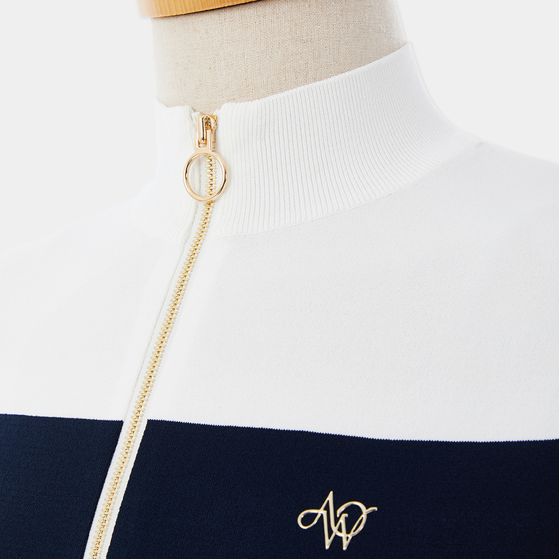 Close-up of a white and navy striped sweater with a gold chain and logo on a mannequin.