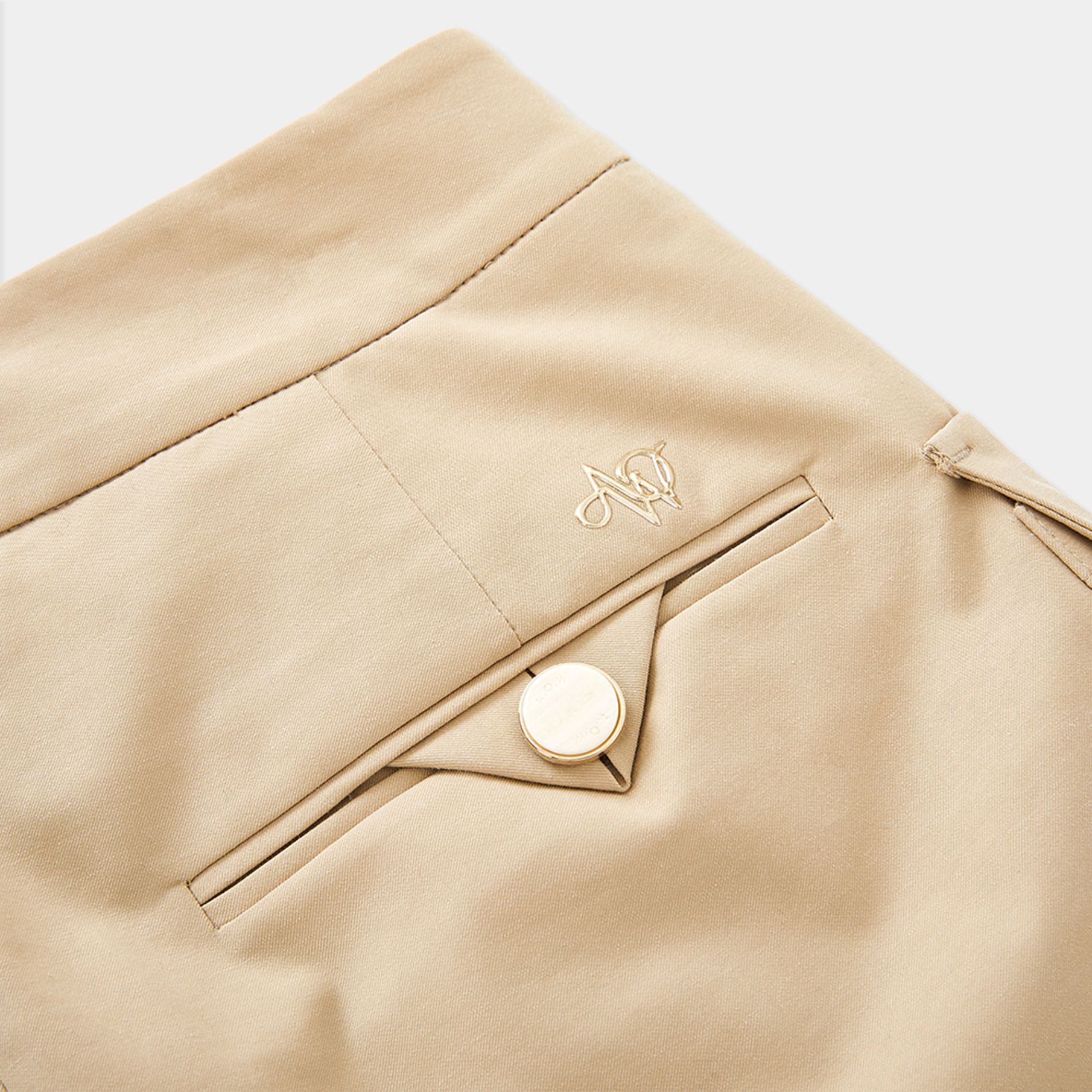 Close-up of beige skirt with a button and brand logo on a white background