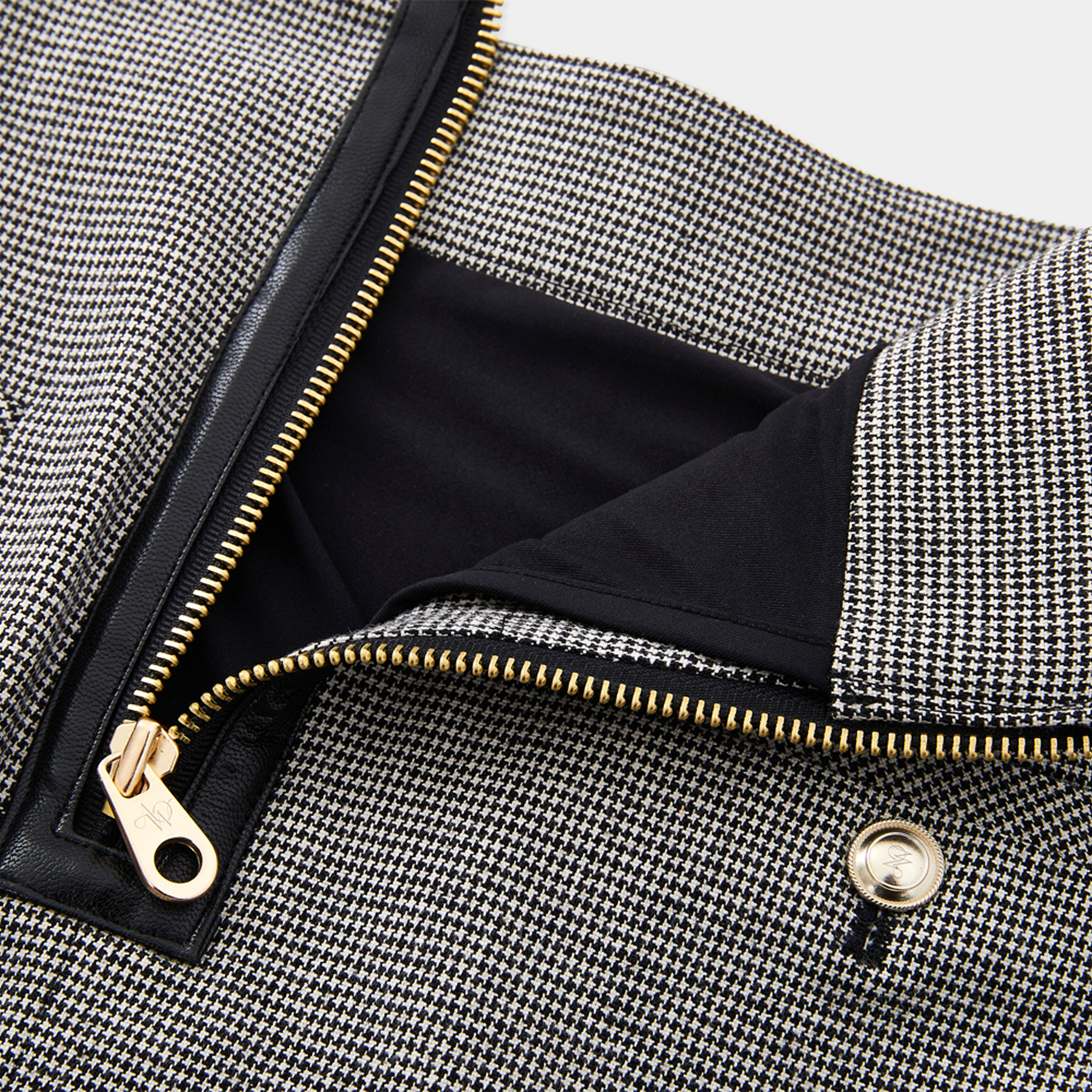 Close-up of a black and white houndstooth patterned skirt with a gold zipper.