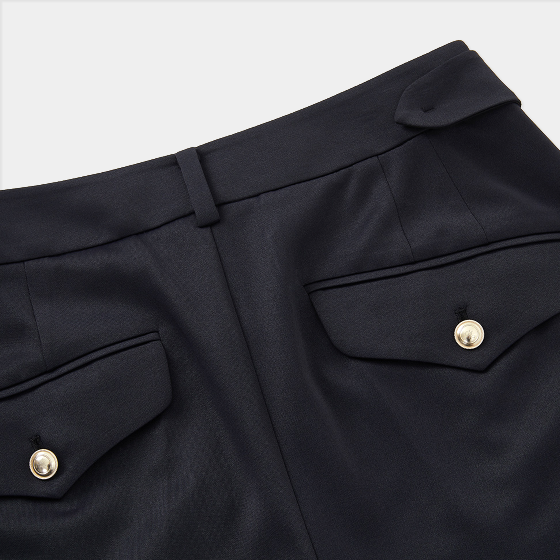 Close-up of black pants with gold buttons on a white background