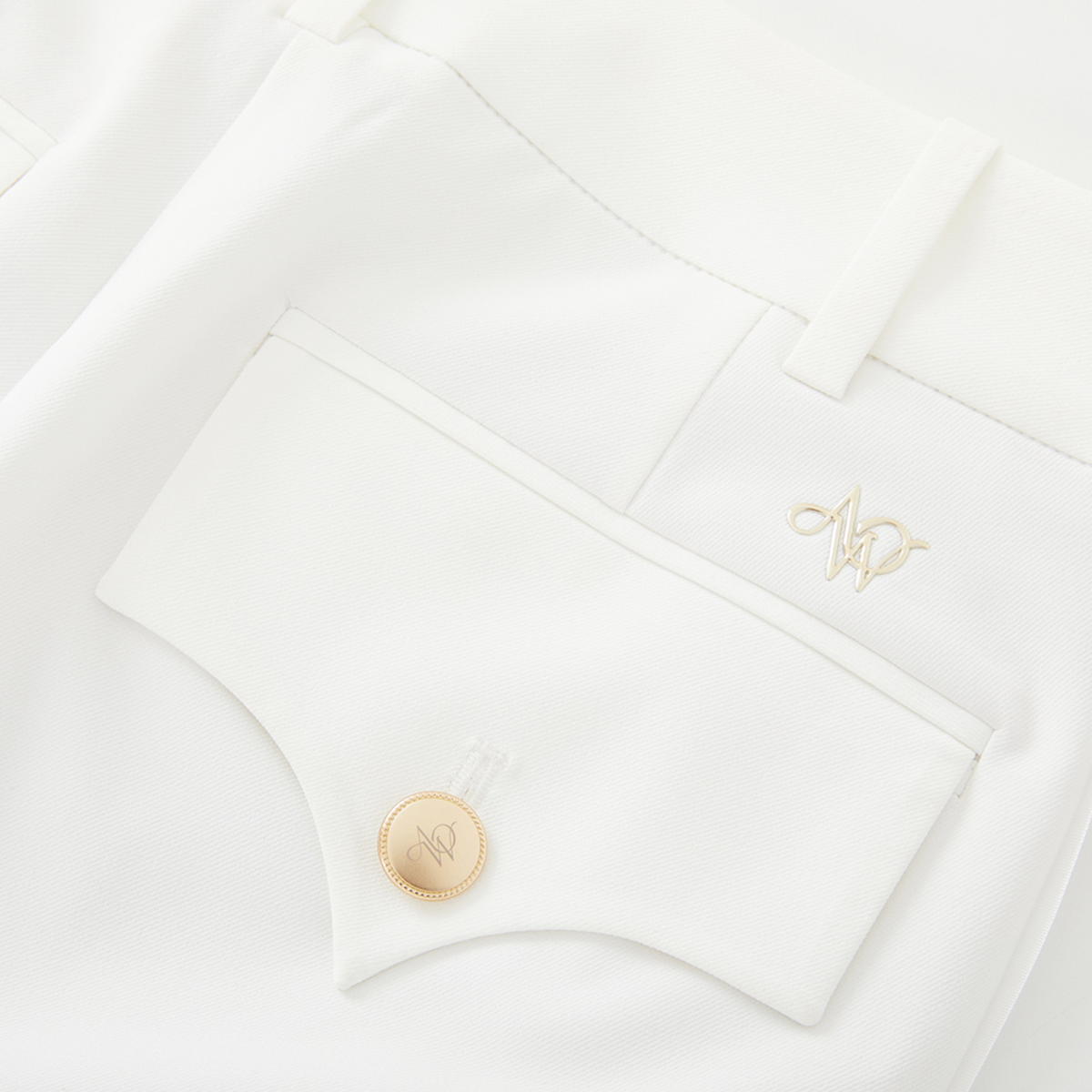 Close-up of a white pants with a gold button and embroidered initials on a white background
