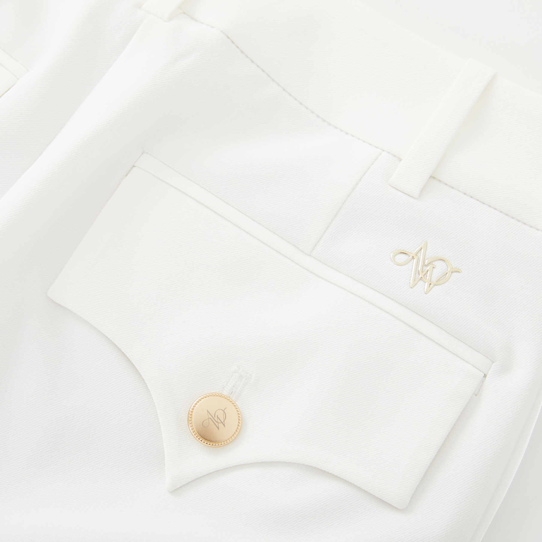 Close-up of a white pants with a gold button and embroidered initials on a white background