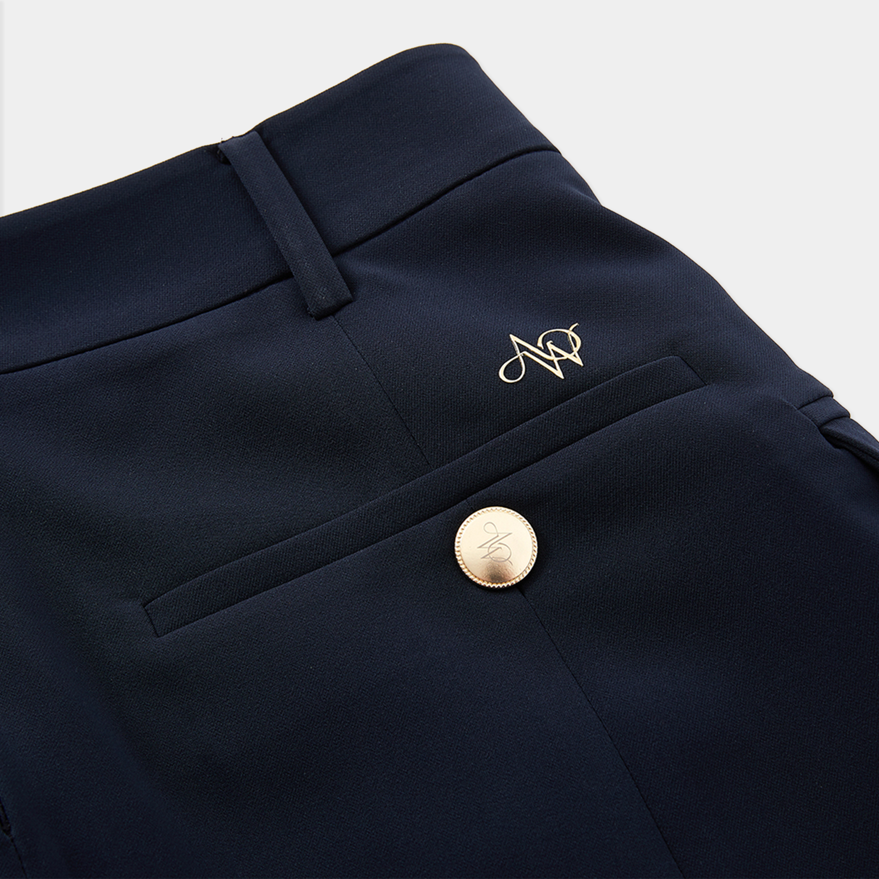 Navy blue pants with a gold button and monogram on a light gray background