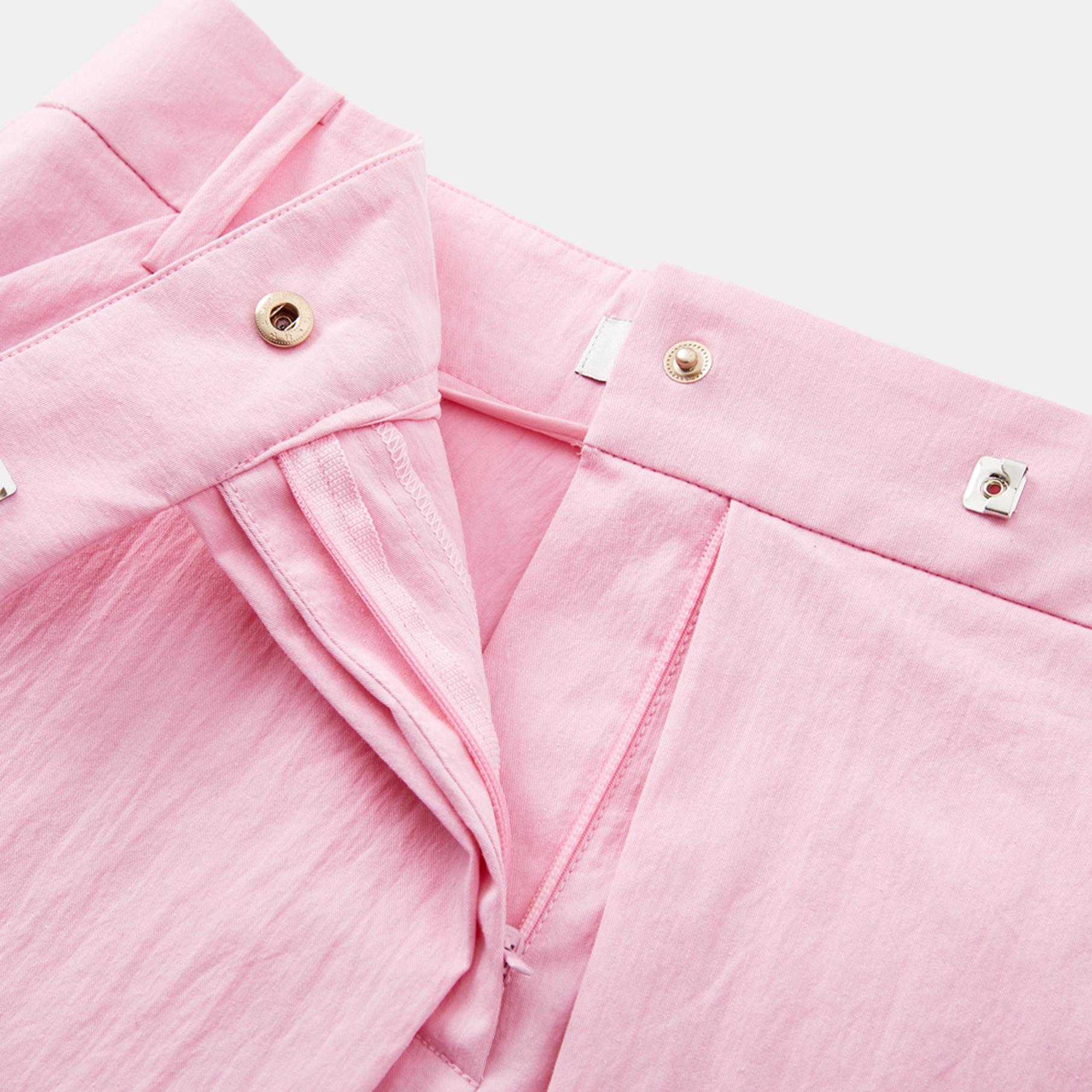 Close-up of pink shorts with gold buttons on a light gray background