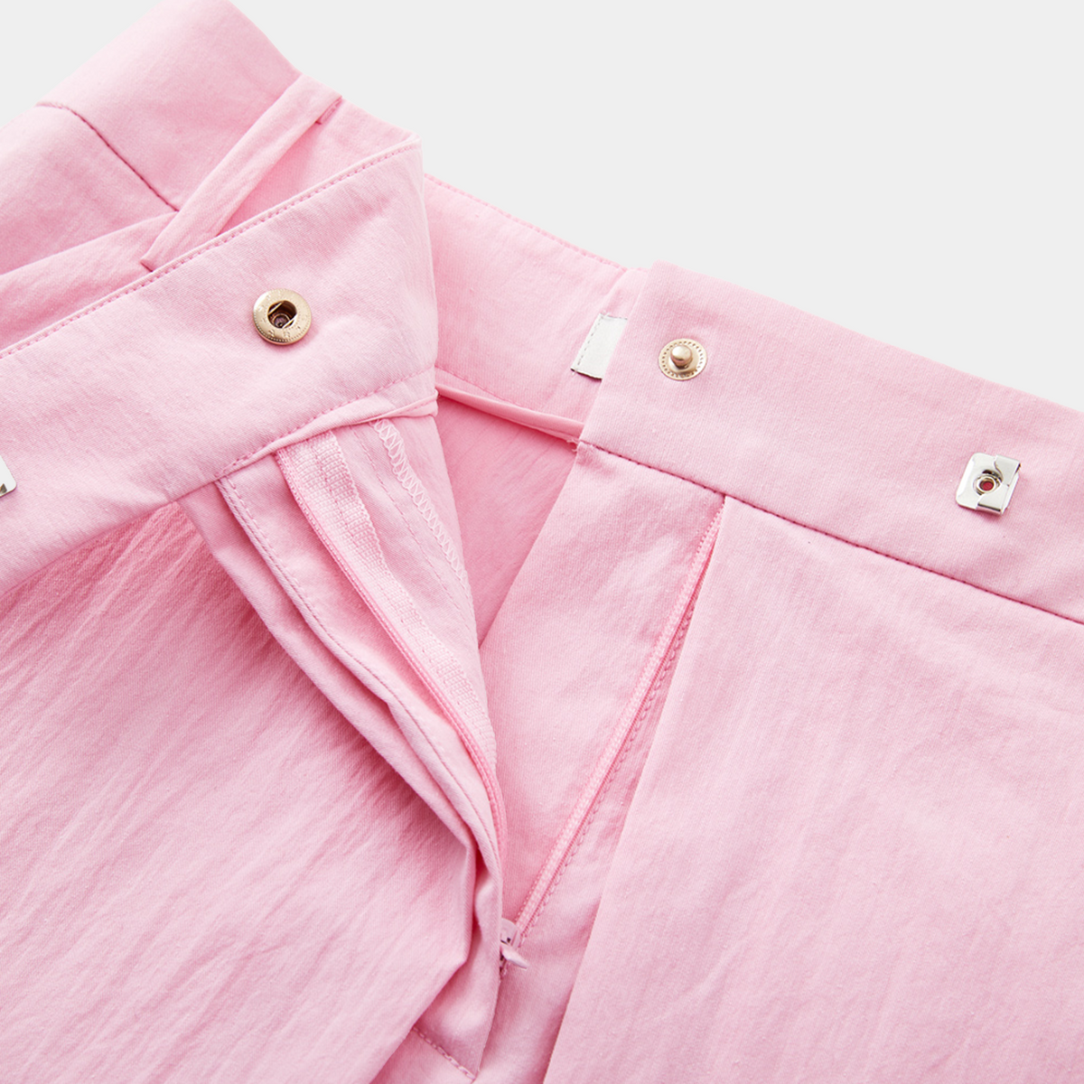Close-up of pink shorts with gold buttons on a light gray background