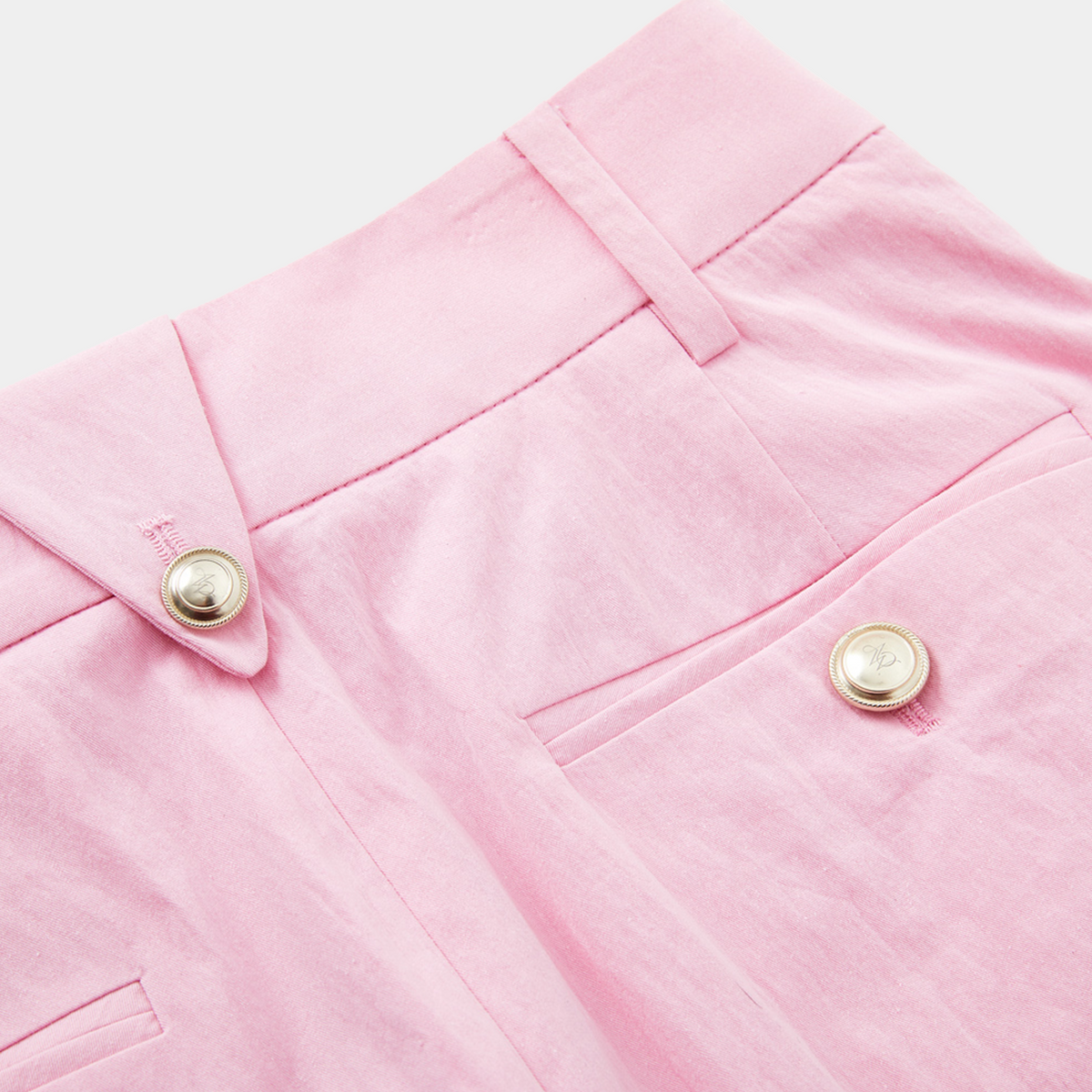 Close-up of pink fabric with gold buttons on a light pink background