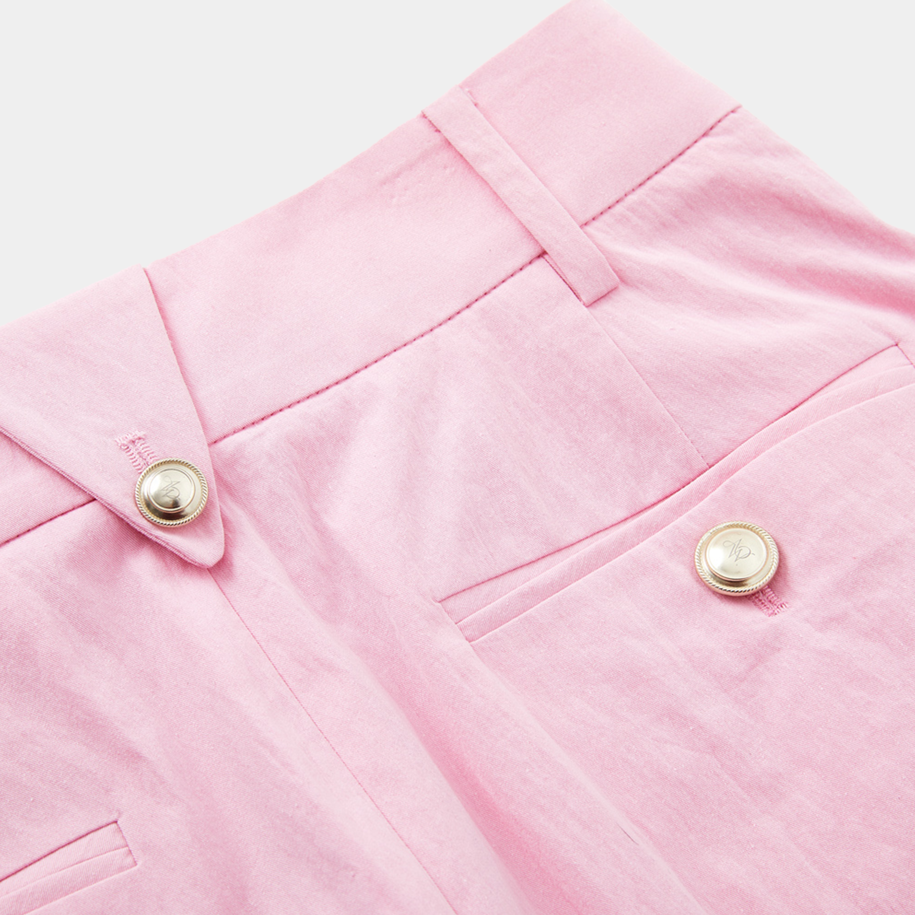 Close-up of pink fabric with gold buttons on a light pink background