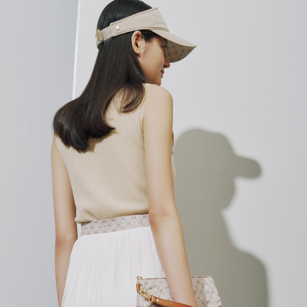A woman shown from the back wearing a beige visor with a patterned brim, a beige ribbed sleeveless top, and a white skirt, holding a matching patterned clutch bag against a light gray wall.