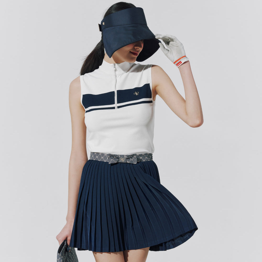 A model wearing a sleeveless white knit top with navy blue horizontal stripes, a pleated navy blue skirt, a patterned belt, a navy visor, and a white glove, posed against a light gray studio background.