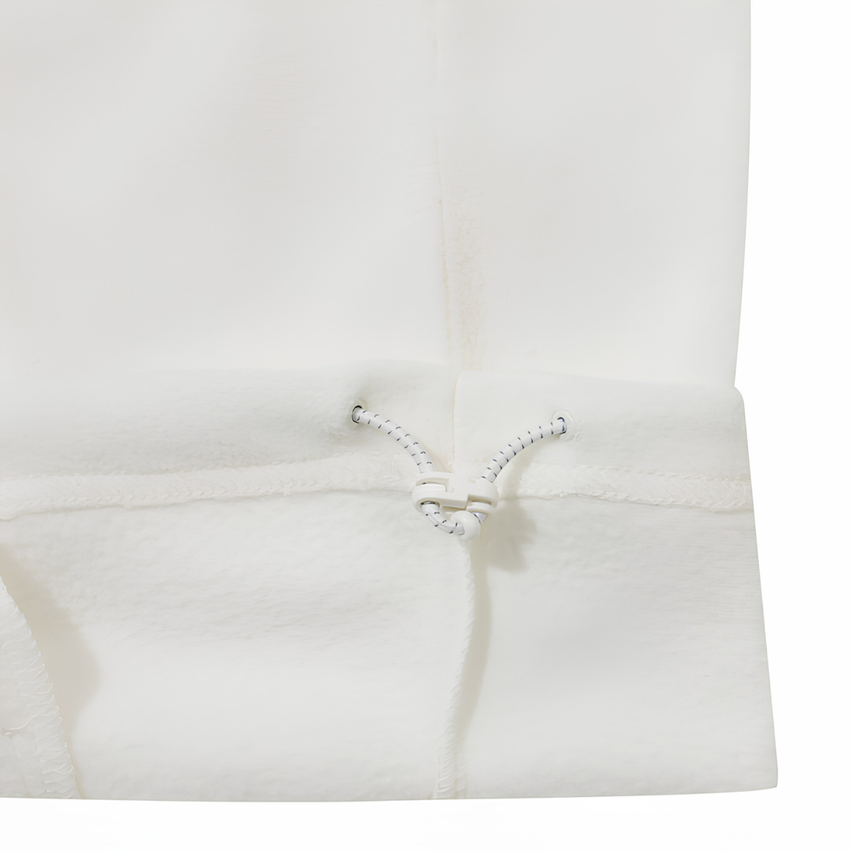 Close-up detail of a white fleece garment, showing the soft texture, a stitched seam, and a white drawstring closure with black speckles.