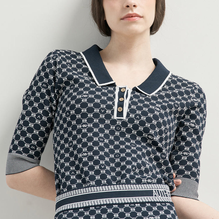 A woman wearing a navy and white patterned short-sleeve polo shirt with a double collar and button placket, photographed against a plain light gray background.