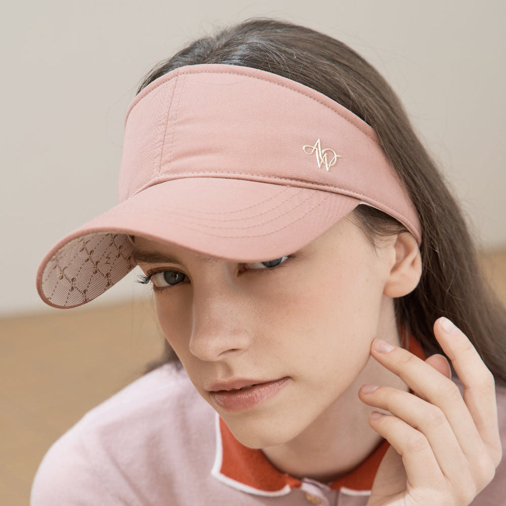 A woman wearing a dusty pink visor with a small silver embroidered logo and a matching pink long-sleeve top with orange trim.