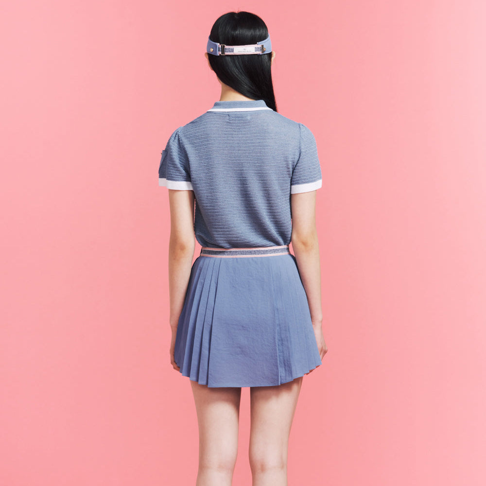 A woman viewed from behind wearing a short-sleeve blue pleated mini dress with white trim on the collar and sleeve cuffs, set against a solid pink background.
