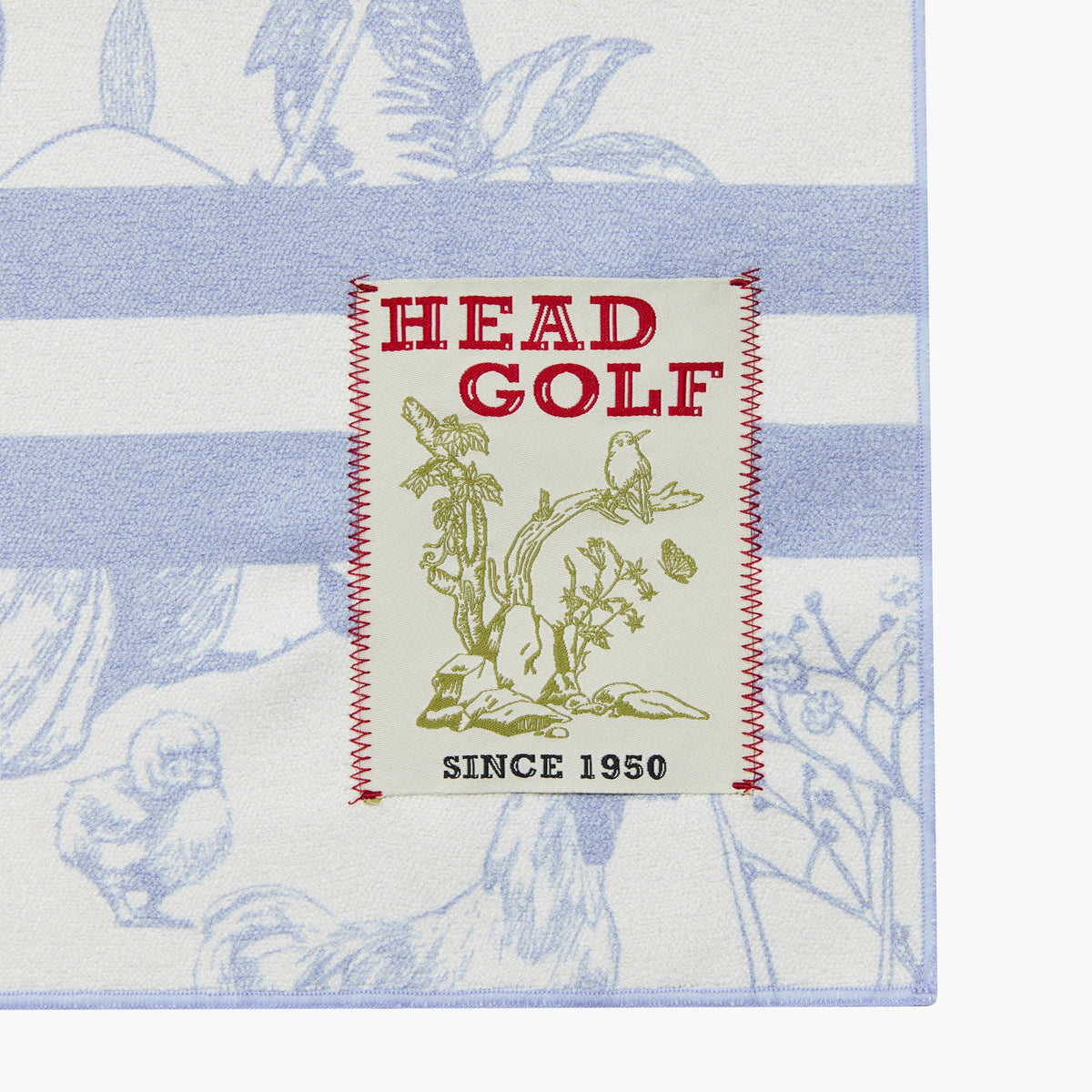 Close-up of a square golf towel or mat with a white base, light blue botanical stripes, and a central cream patch reading 'HEAD GOLF' with red stitching and green illustration. The product fills most of the frame against a white background.