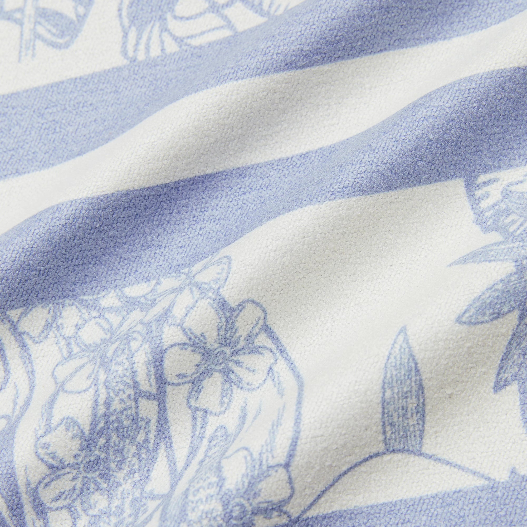 A close-up of a fabric or textile surface with a blue and off-white pattern, showing floral and botanical line art over broad blue bands.