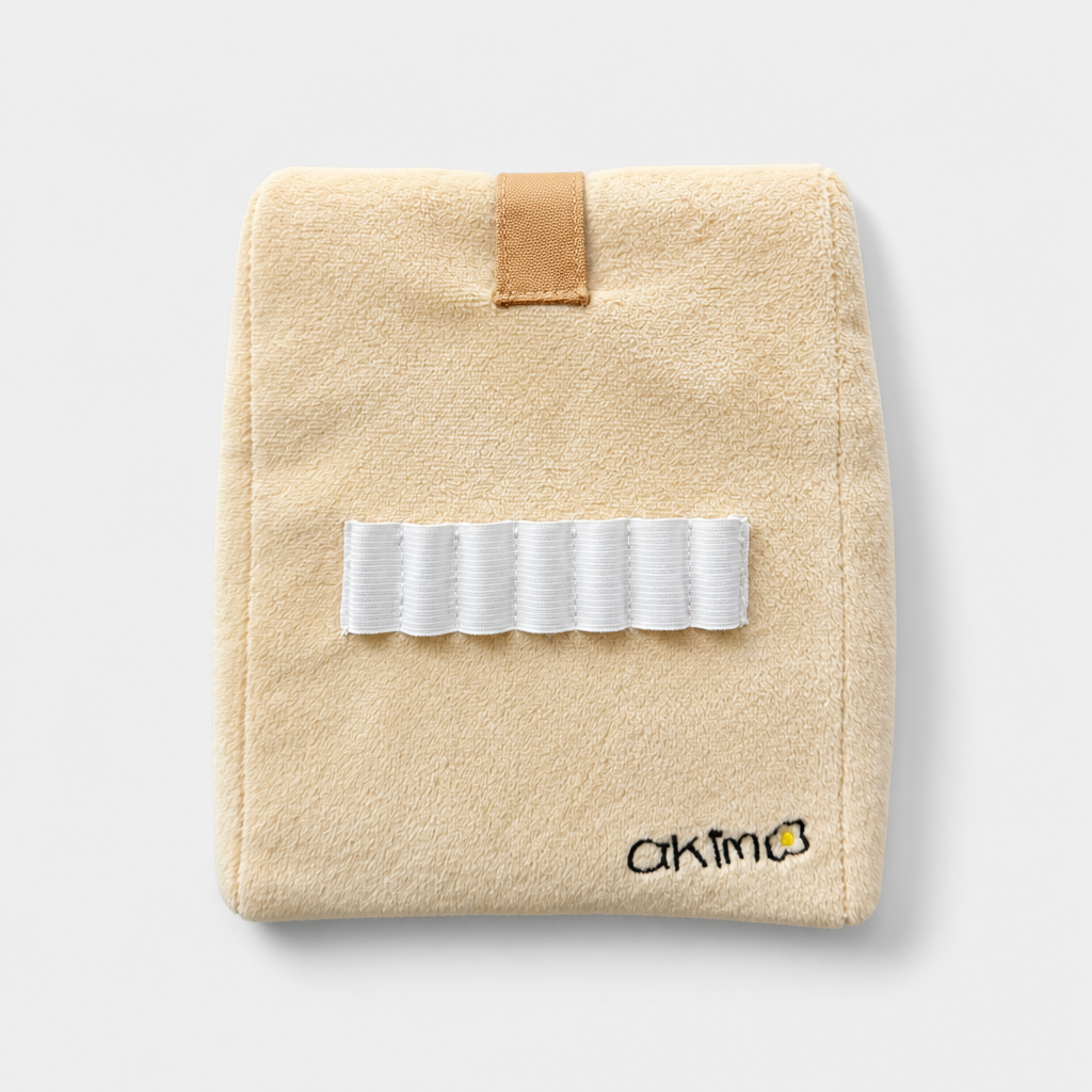 A beige head cover with a white elastic band across the front, a tan loop tab at the top, and a small black embroidered logo reading 'akim' near the bottom right, shown on a light gray background.