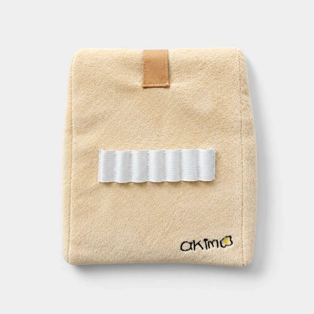 A beige head cover with a white elastic band across the front, a tan loop tab at the top, and a small black embroidered logo reading 'akima' near the bottom right, shown on a light gray background.