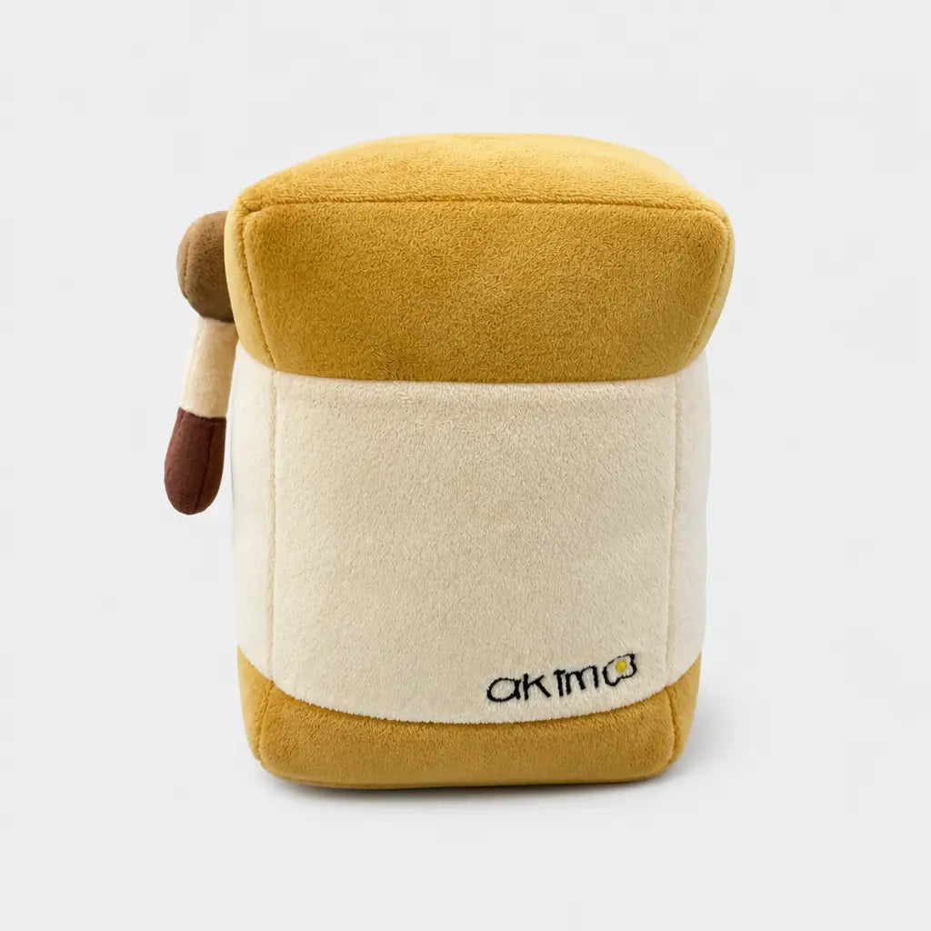 A plush driver cover, featuring a mustard yellow top and bottom, a cream-colored center, and a small brown tail on the left side. The Akima brand logo is embroidered on the bottom right.