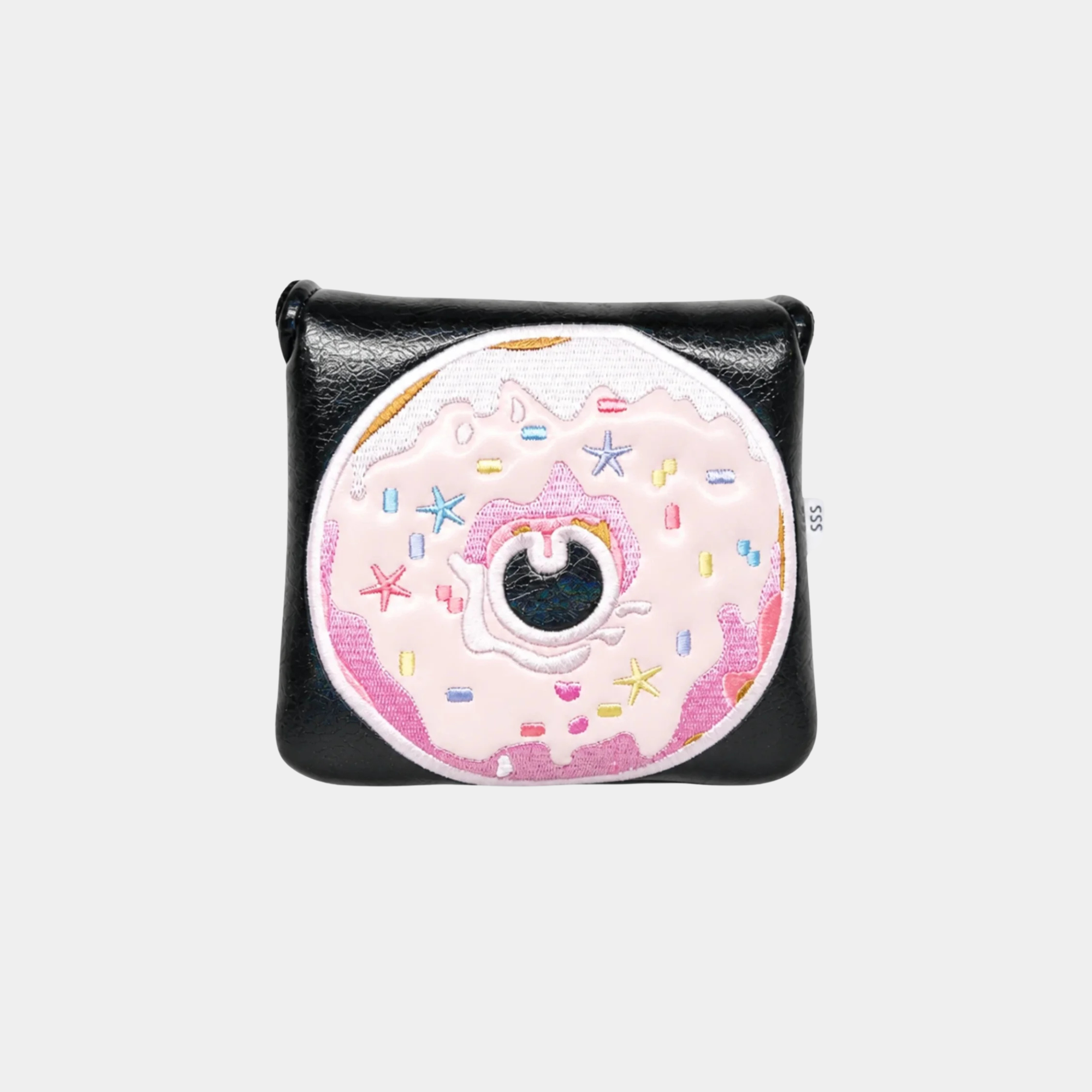 A black leather mallet putter cover featuring a large, circular, embroidered donut patch on the front. The donut is light pink with white icing, colorful embroidered sprinkles, and a central black-and-white eye motif.