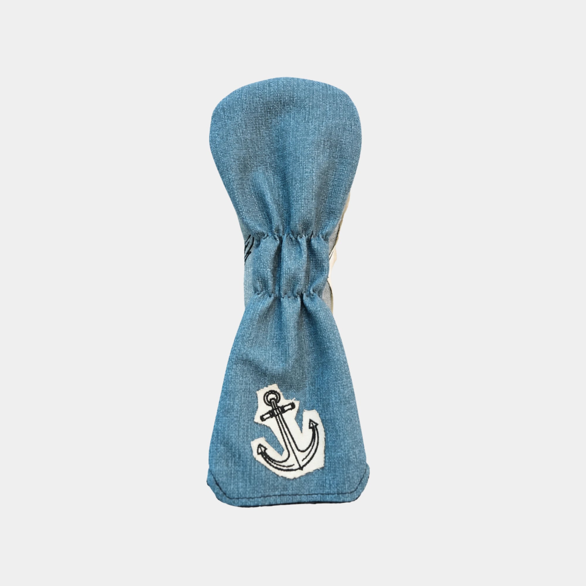 A blue denim golf club headcover with an embroidered white and black anchor on the lower front, shown against a light gray background.