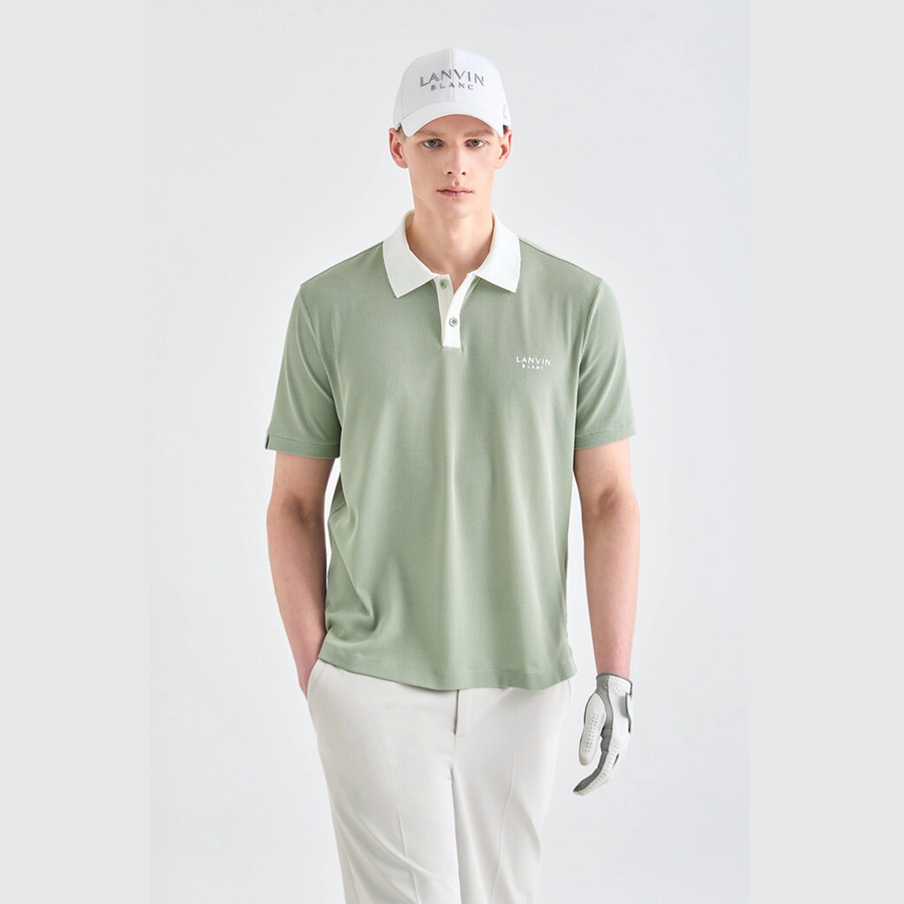 Man wearing a green polo shirt with white collar and 'LANVIN' branding, white pants, and a white cap on a light gray background.