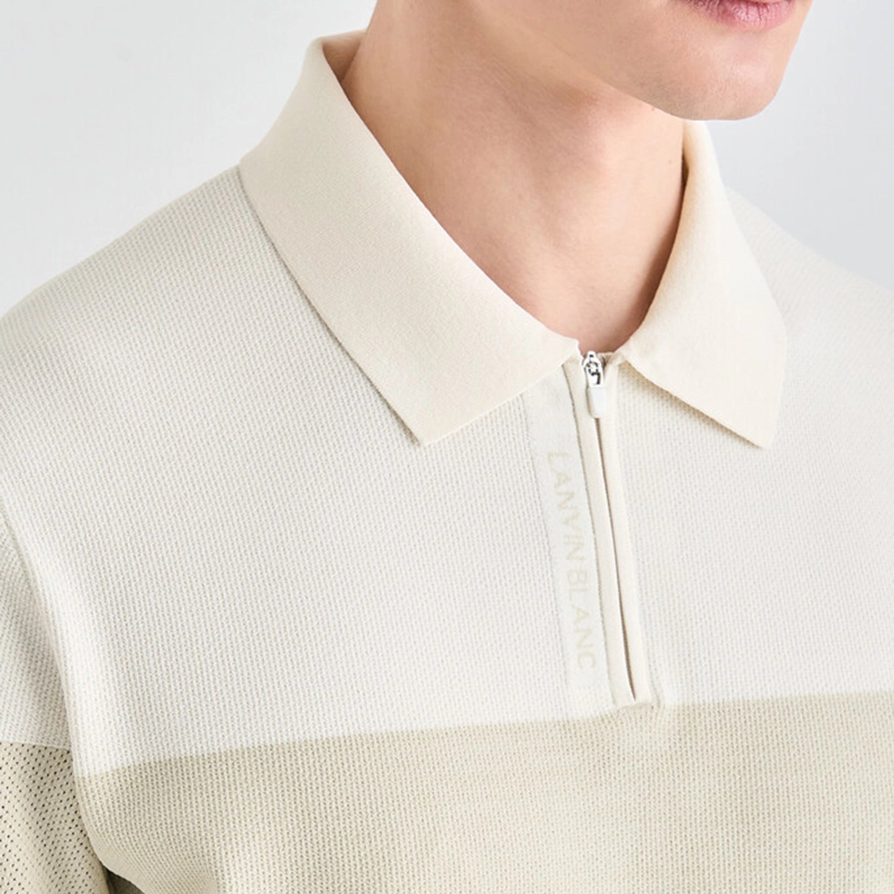 Close-up of a person wearing a cream-colored sweater with a zipper detail.