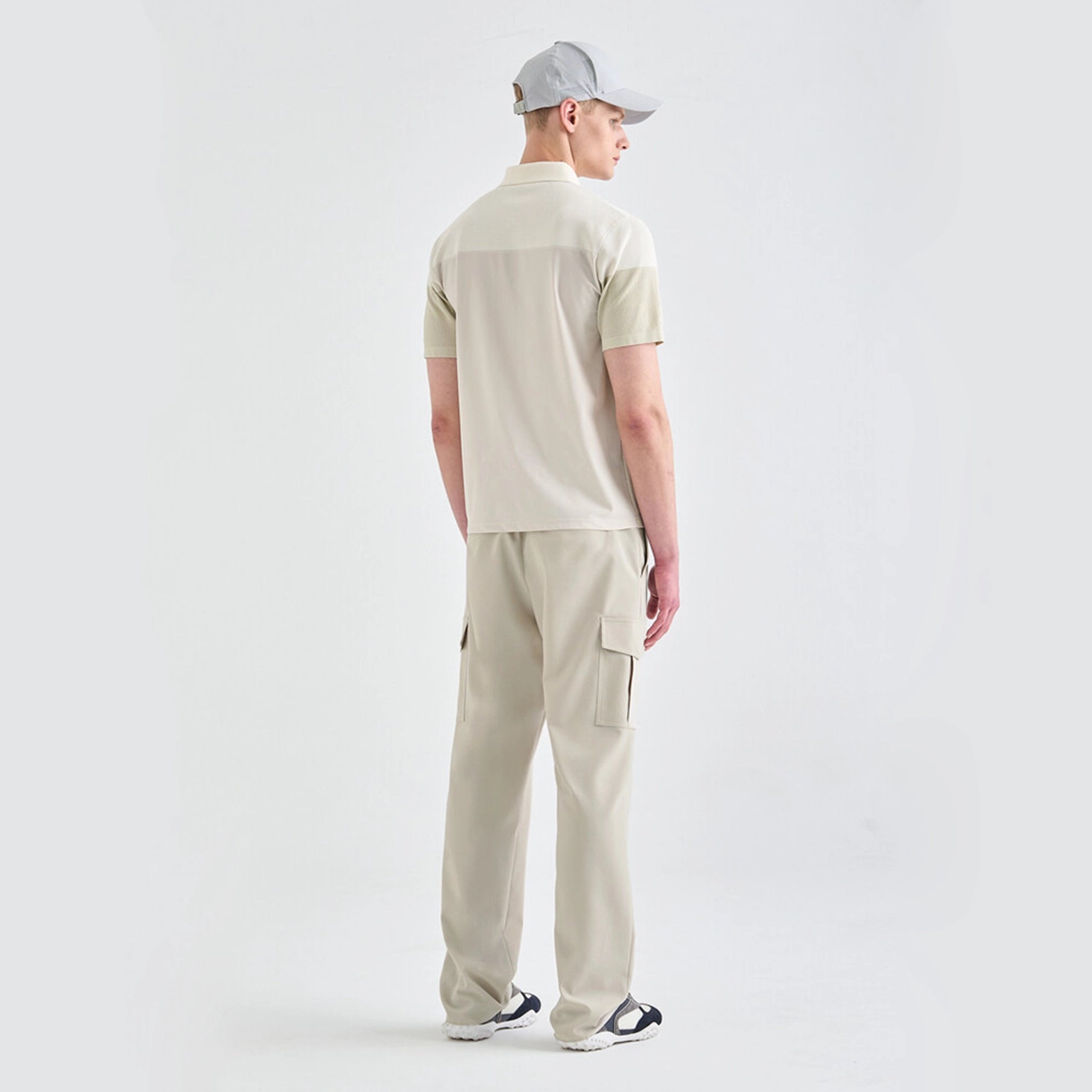 Man wearing a beige polo shirt and pants with a cap on a white background