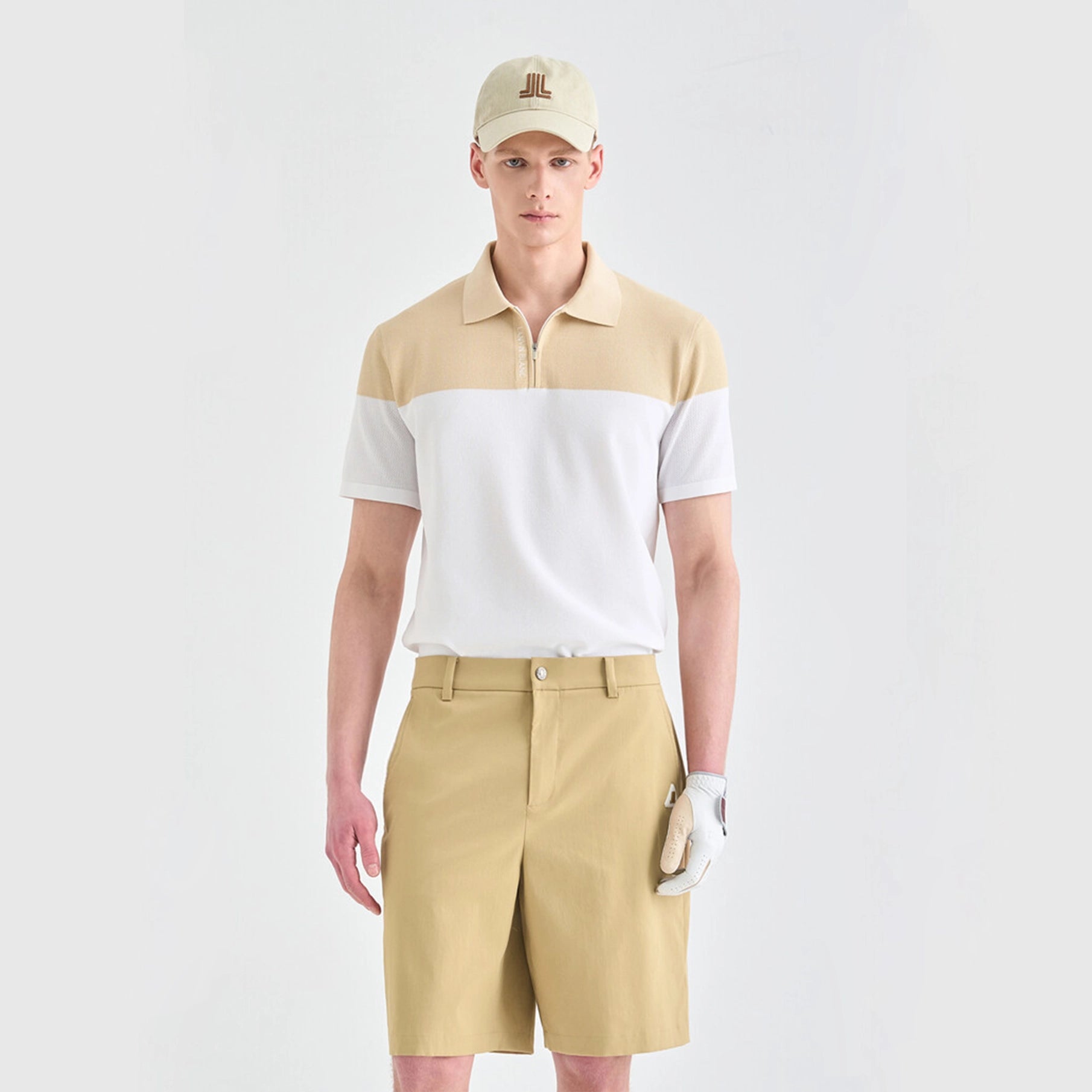 Man wearing a beige and white polo shirt with khaki shorts on a light gray background