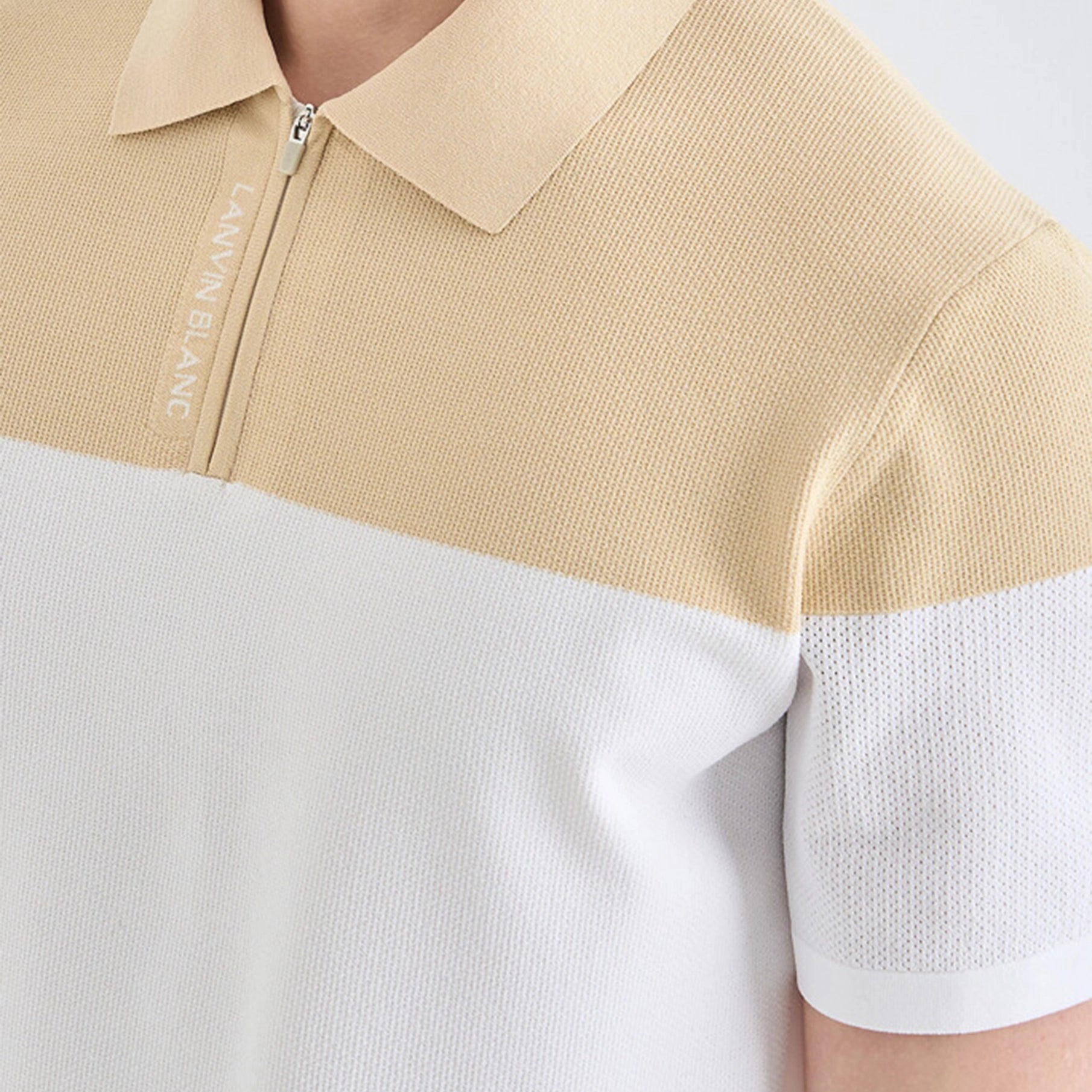 Beige and white polo shirt with brand logo on a light gray background