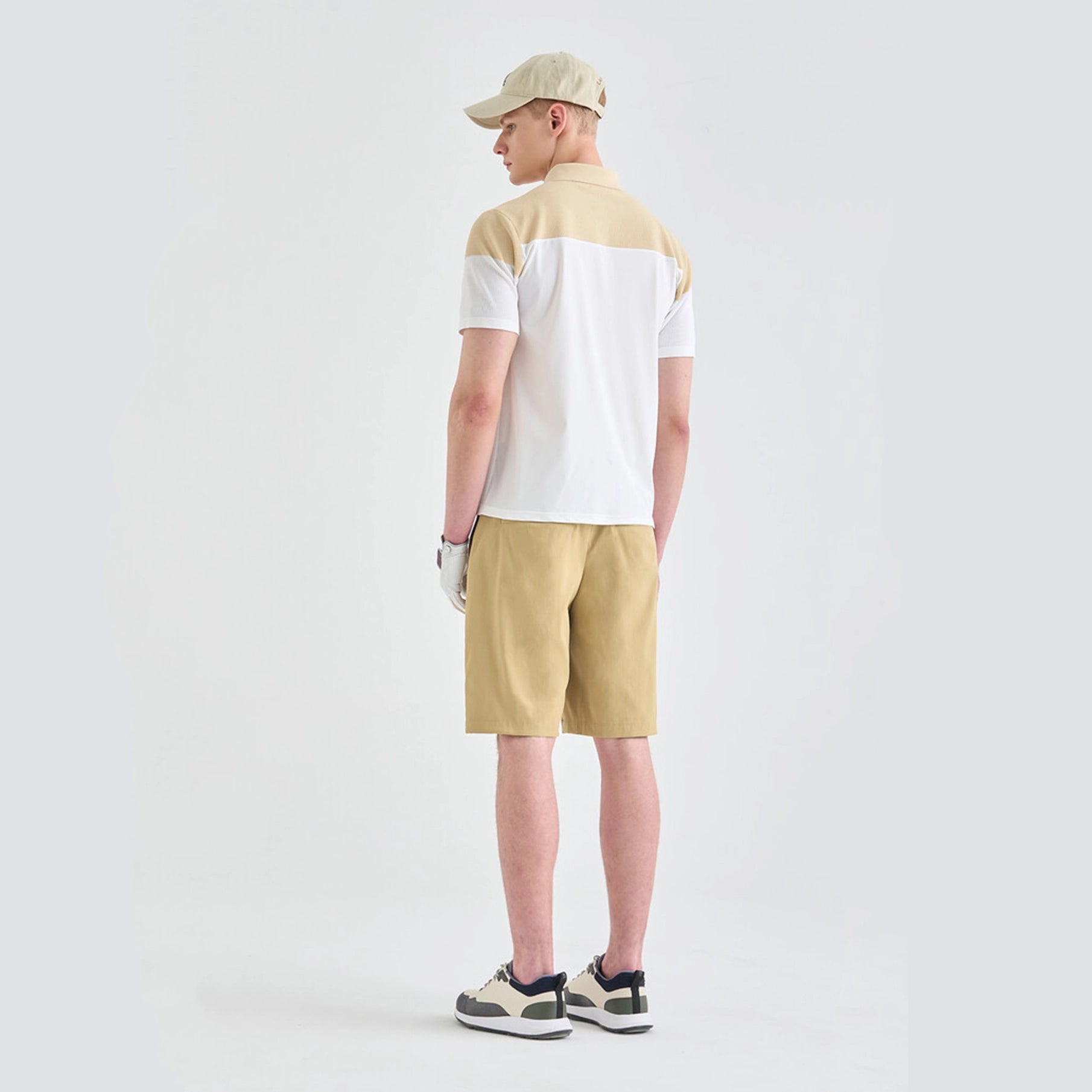 Person wearing a beige and white shirt, beige shorts, and a cap on a light gray background