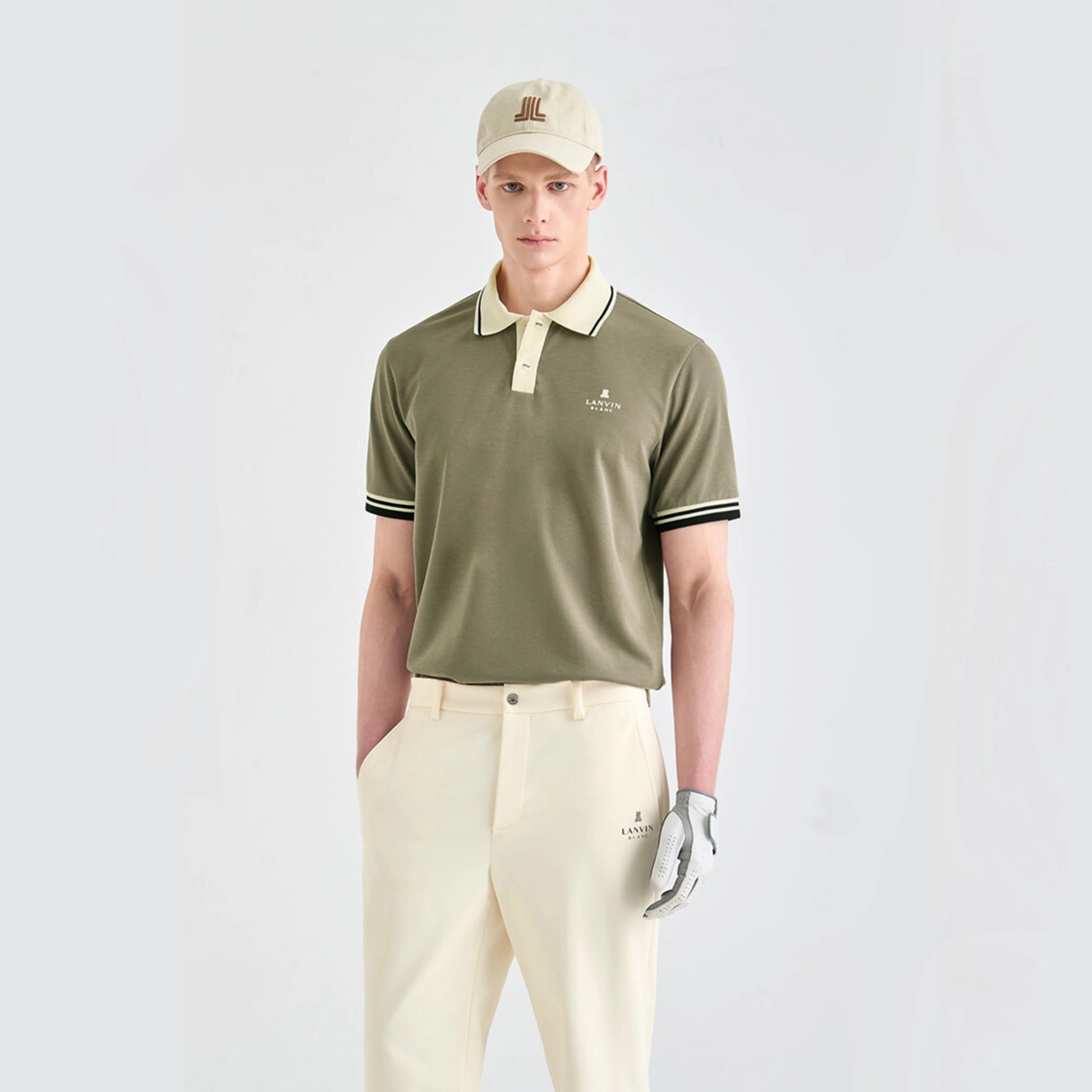 Man wearing a green polo shirt, beige cap, and white pants with a golf glove on a light gray background