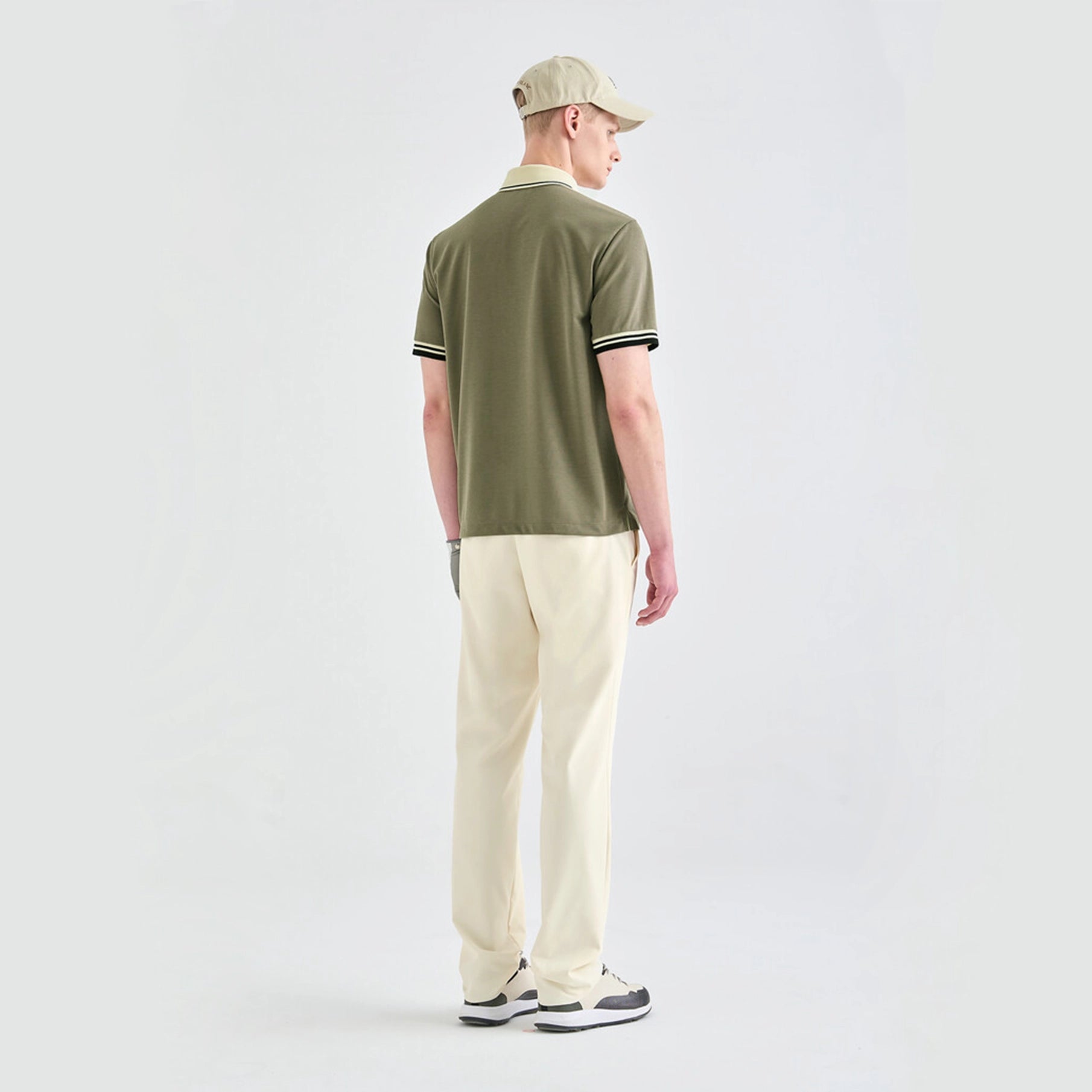 Man wearing a green polo shirt and beige pants on a white background
