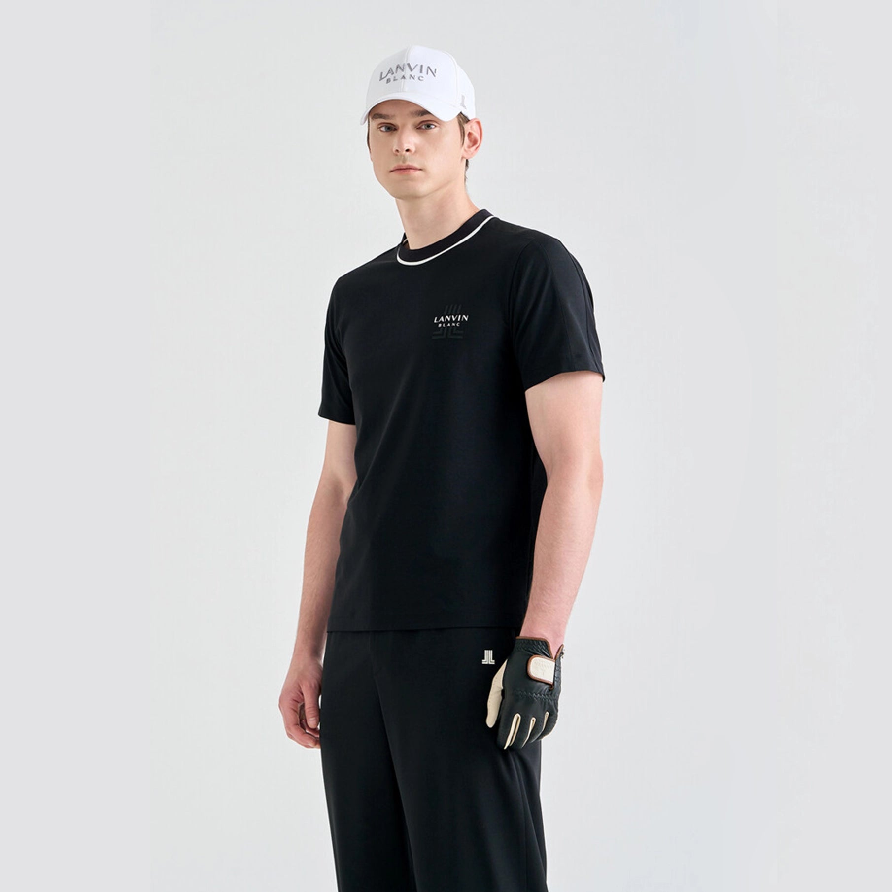 Man wearing a black t-shirt, black pants, and a white cap with a brand logo on a light gray background