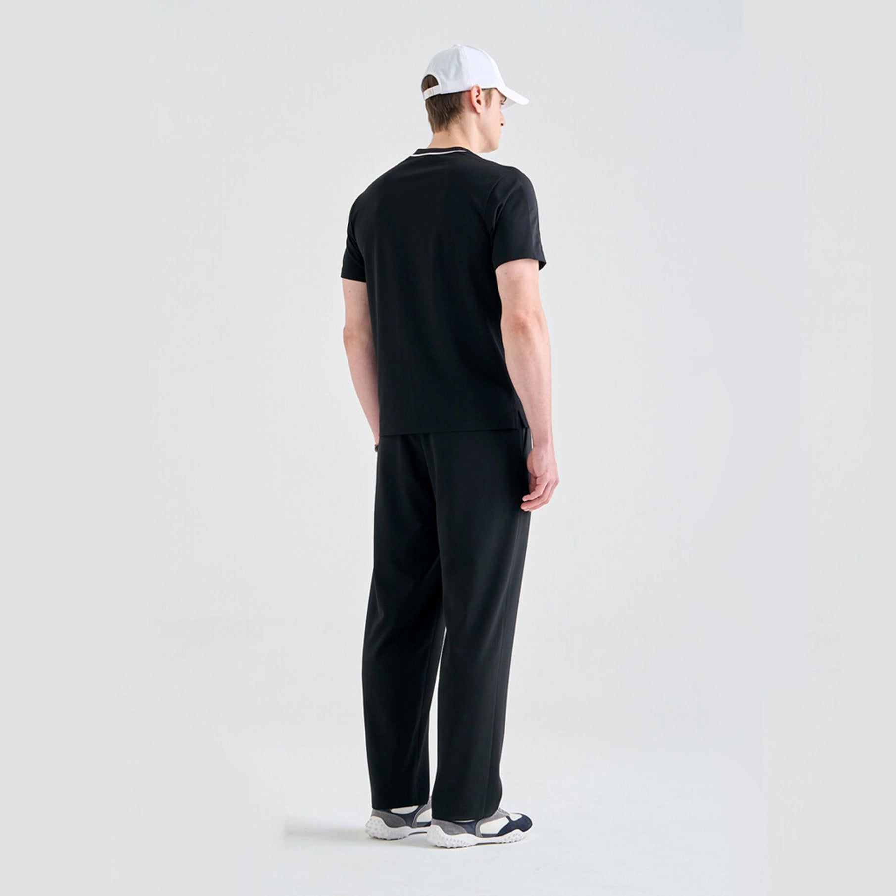Person wearing a black outfit with a white cap on a light gray background