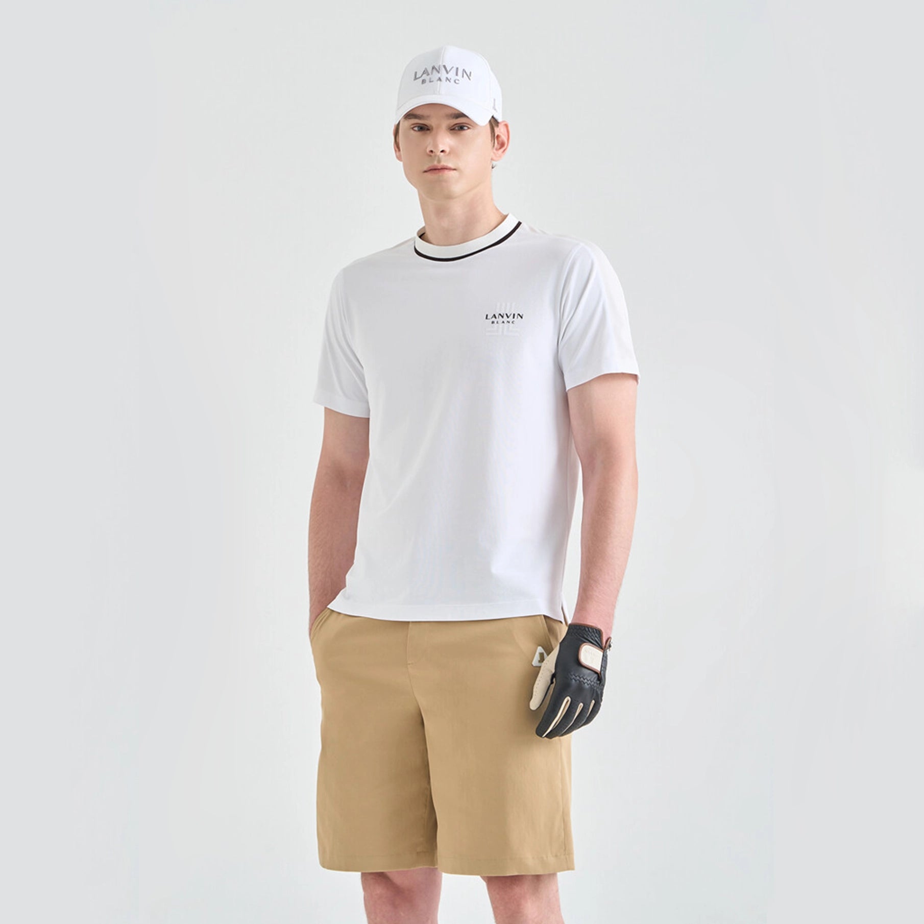 Person wearing a white t-shirt, beige shorts, and a white cap with 'LANVIN' branding on a light gray background.