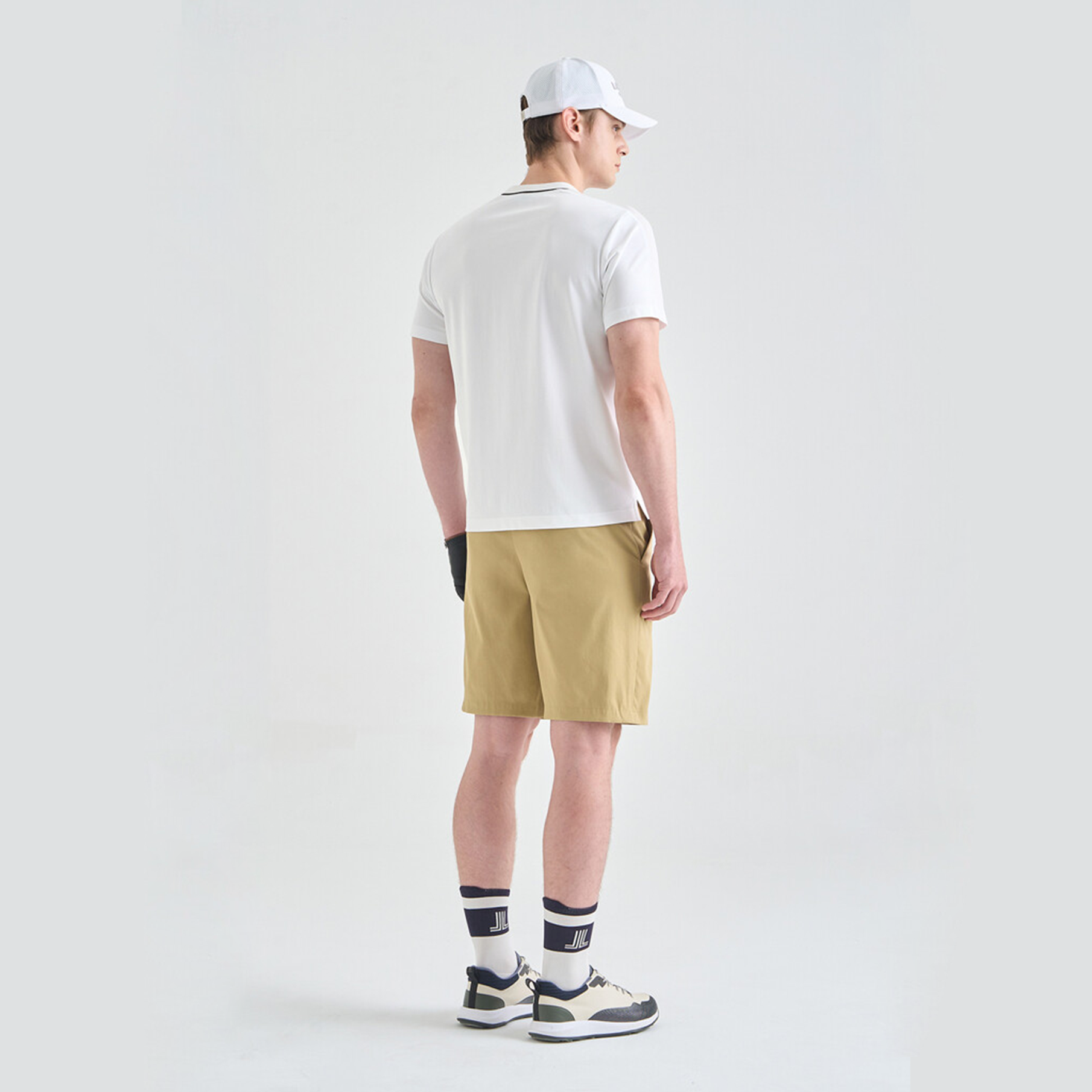 Person wearing a white t-shirt, beige shorts, and black and white sneakers on a light gray background