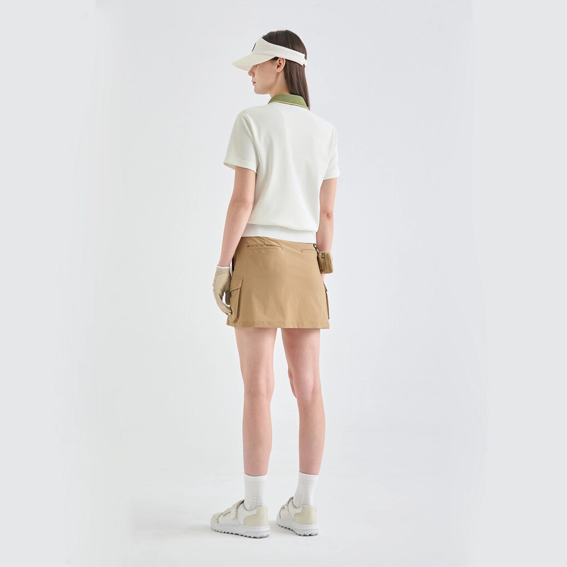 Person wearing a white polo shirt, beige skirt, and visor on a plain background