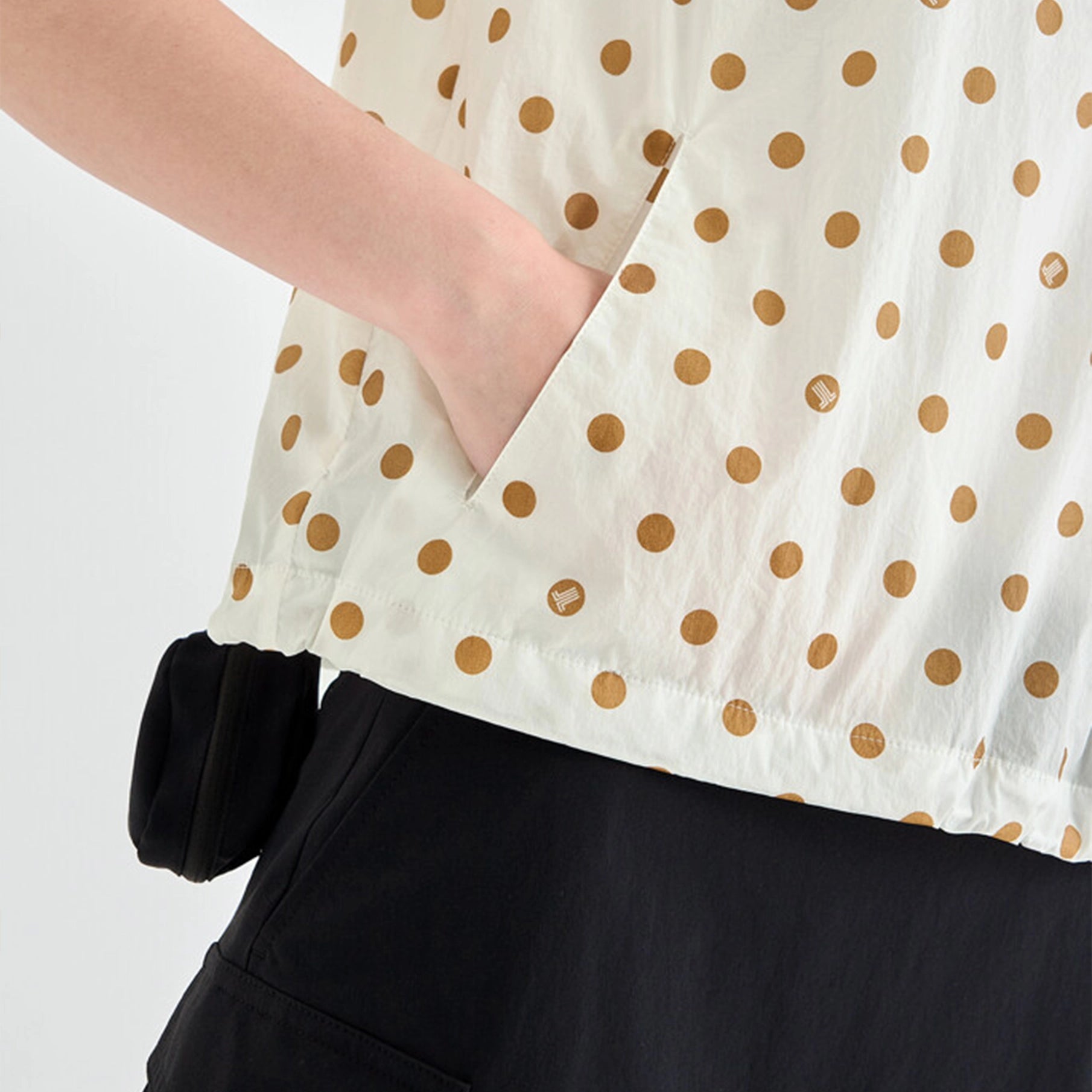 White top with gold polka dots worn by a person on a plain background