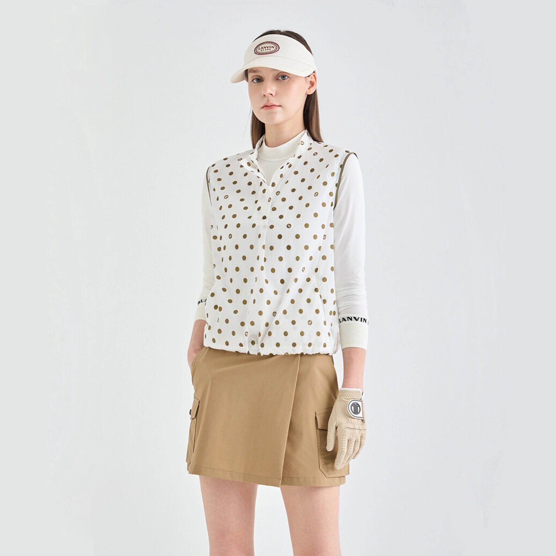 Woman wearing a polka dot golf shirt, beige skirt, and visor on a white background