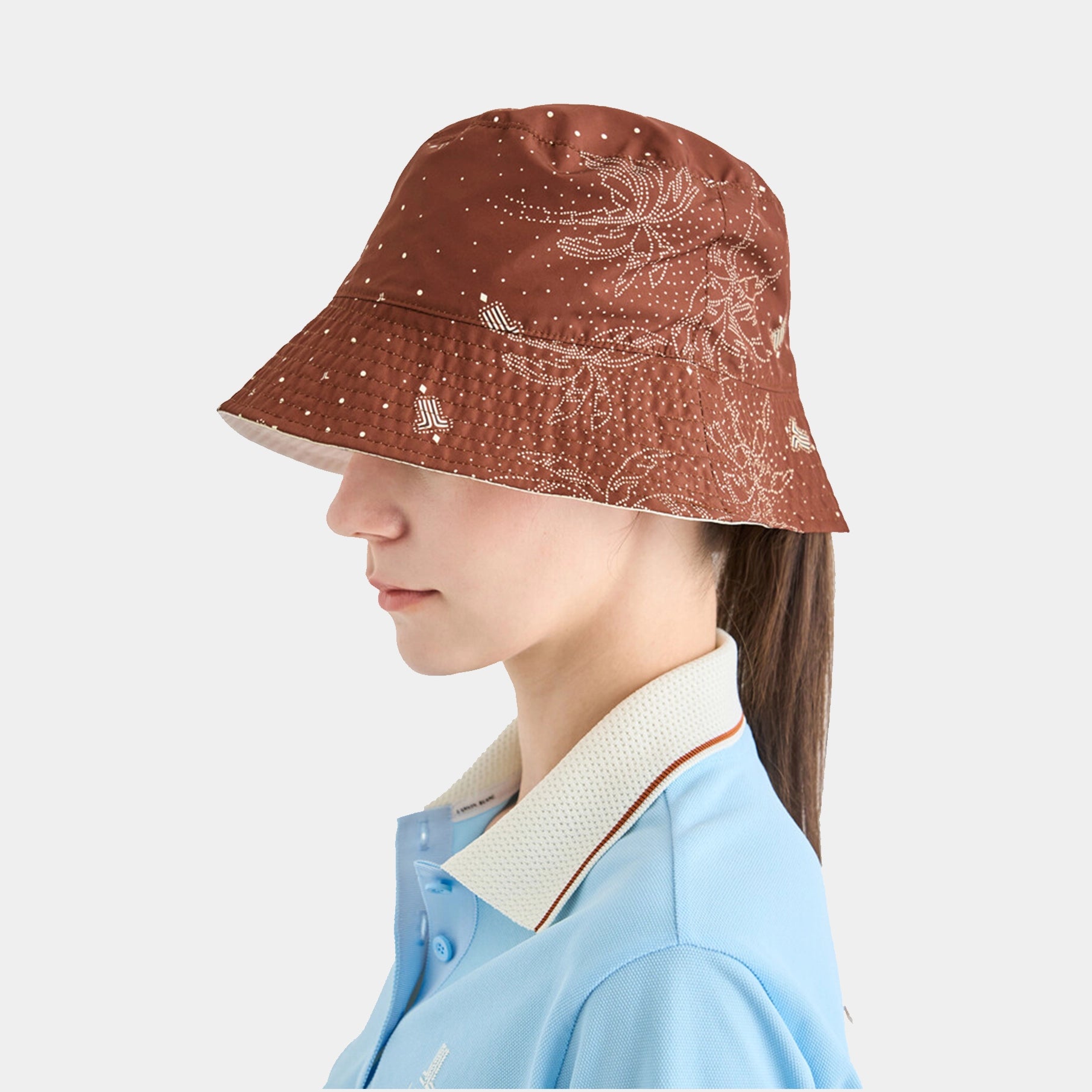 Person wearing a brown patterned bucket hat on a light gray background