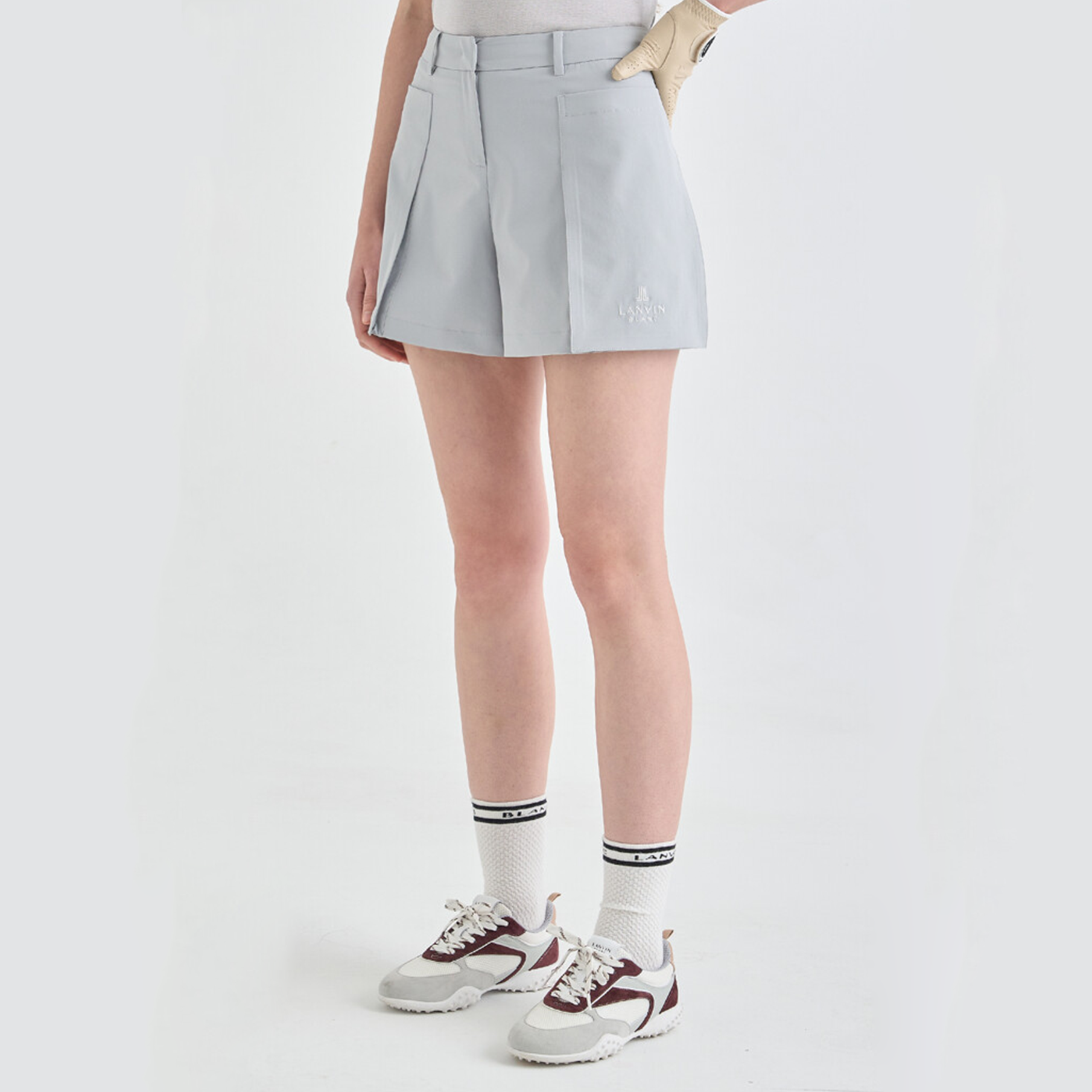 Person wearing a light gray pleated shorts with white sneakers and striped socks on a white background