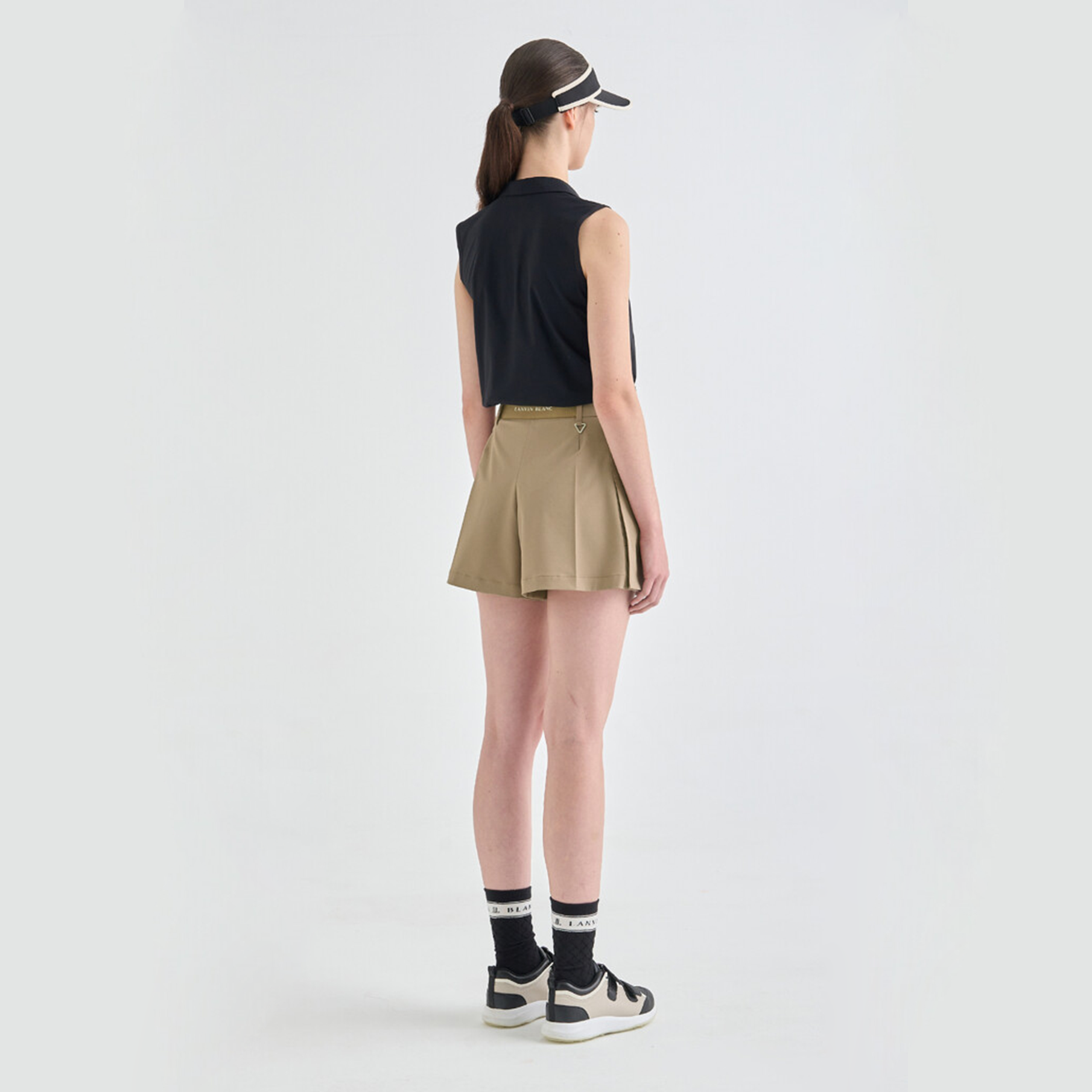 Person wearing a black sleeveless top, beige skirt, and black and white sneakers on a white background