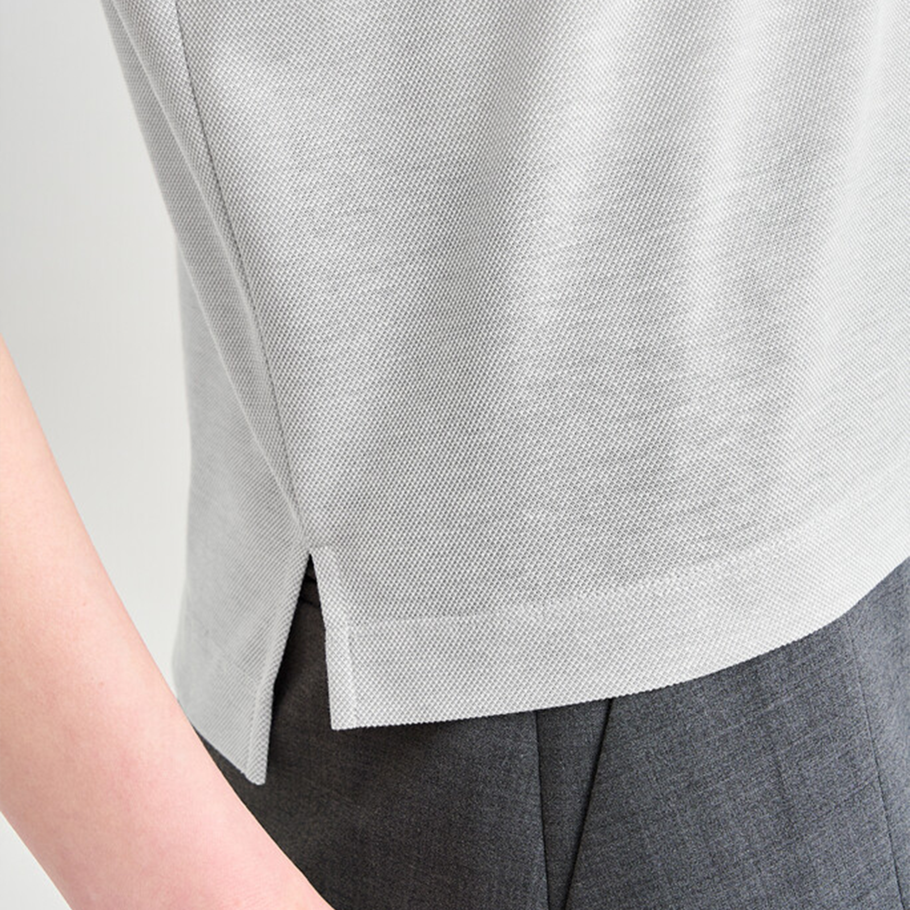 Close-up of a person wearing a light gray polo and dark gray pants against a neutral background