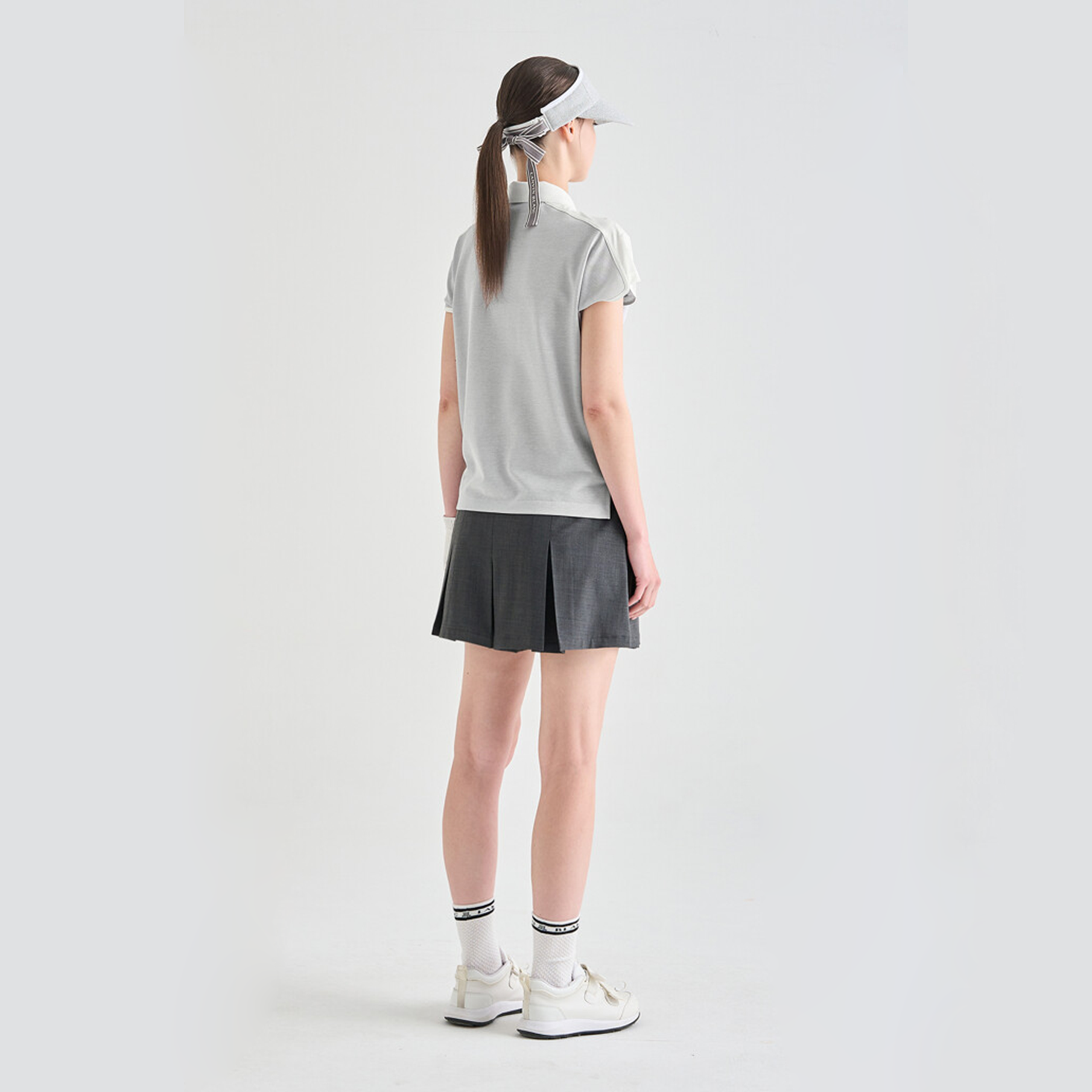 Person wearing a gray polo, black skirt, and white sneakers on a light gray background