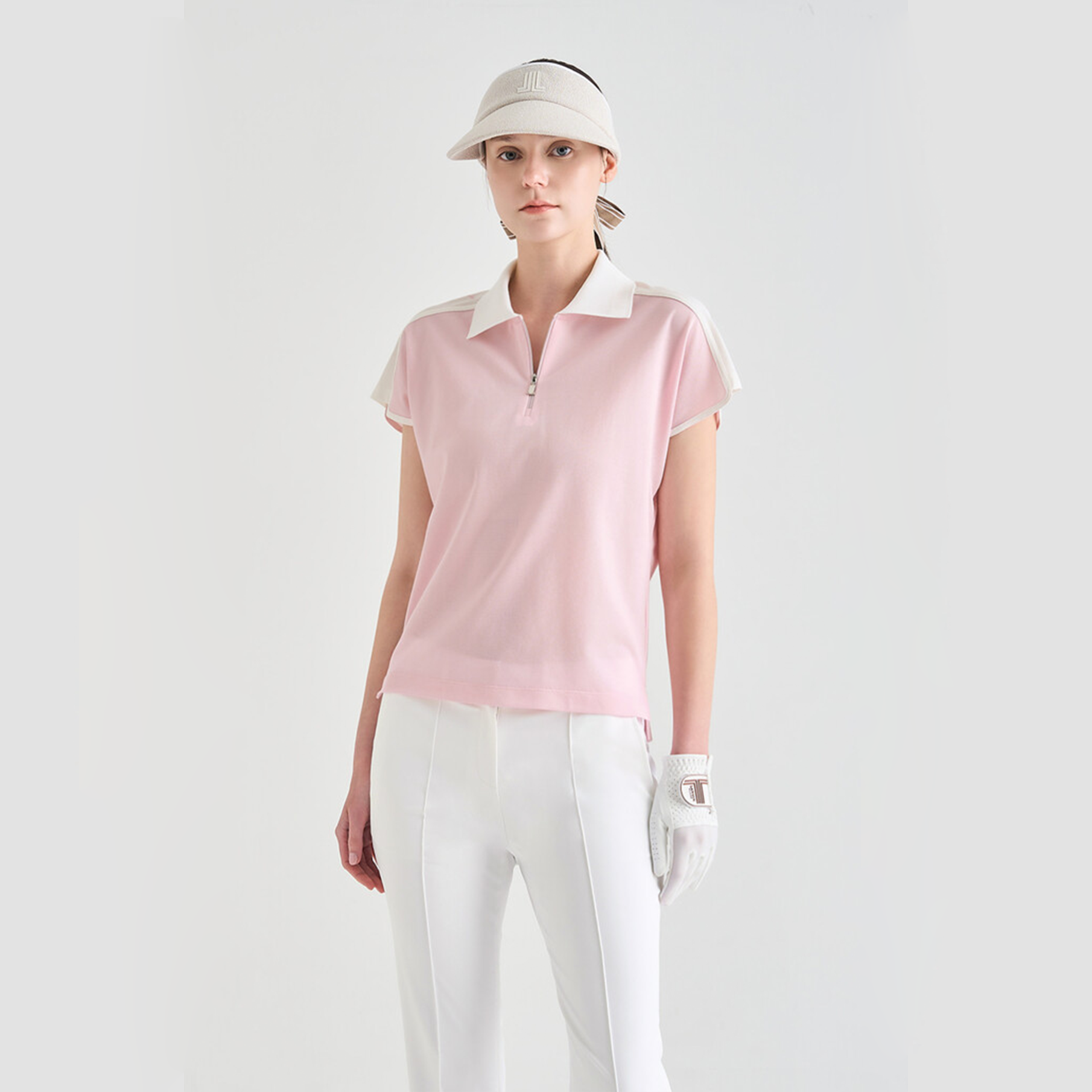 Woman wearing a pink polo shirt and white pants on a light gray background