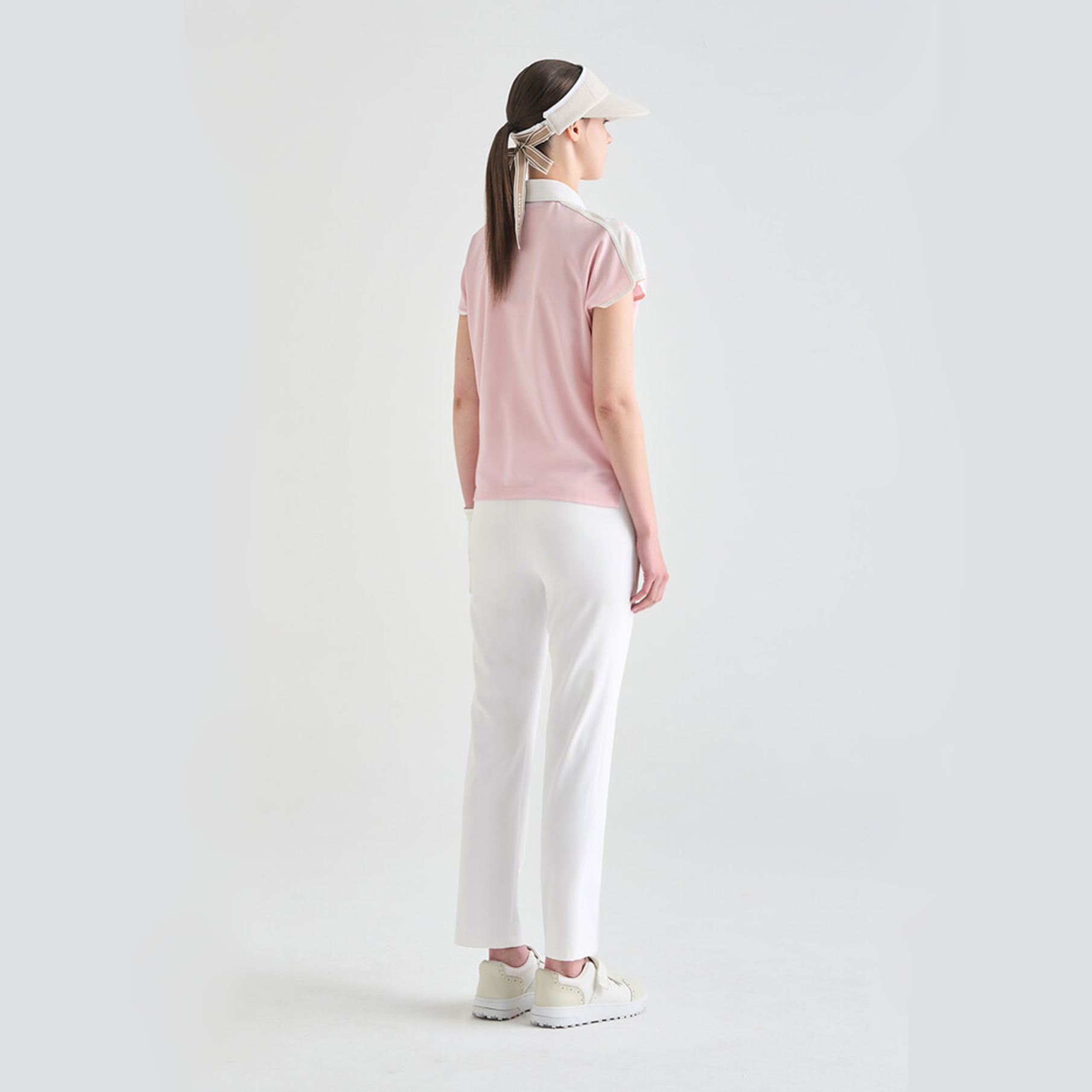 Person wearing a pink top and white pants on a light gray background