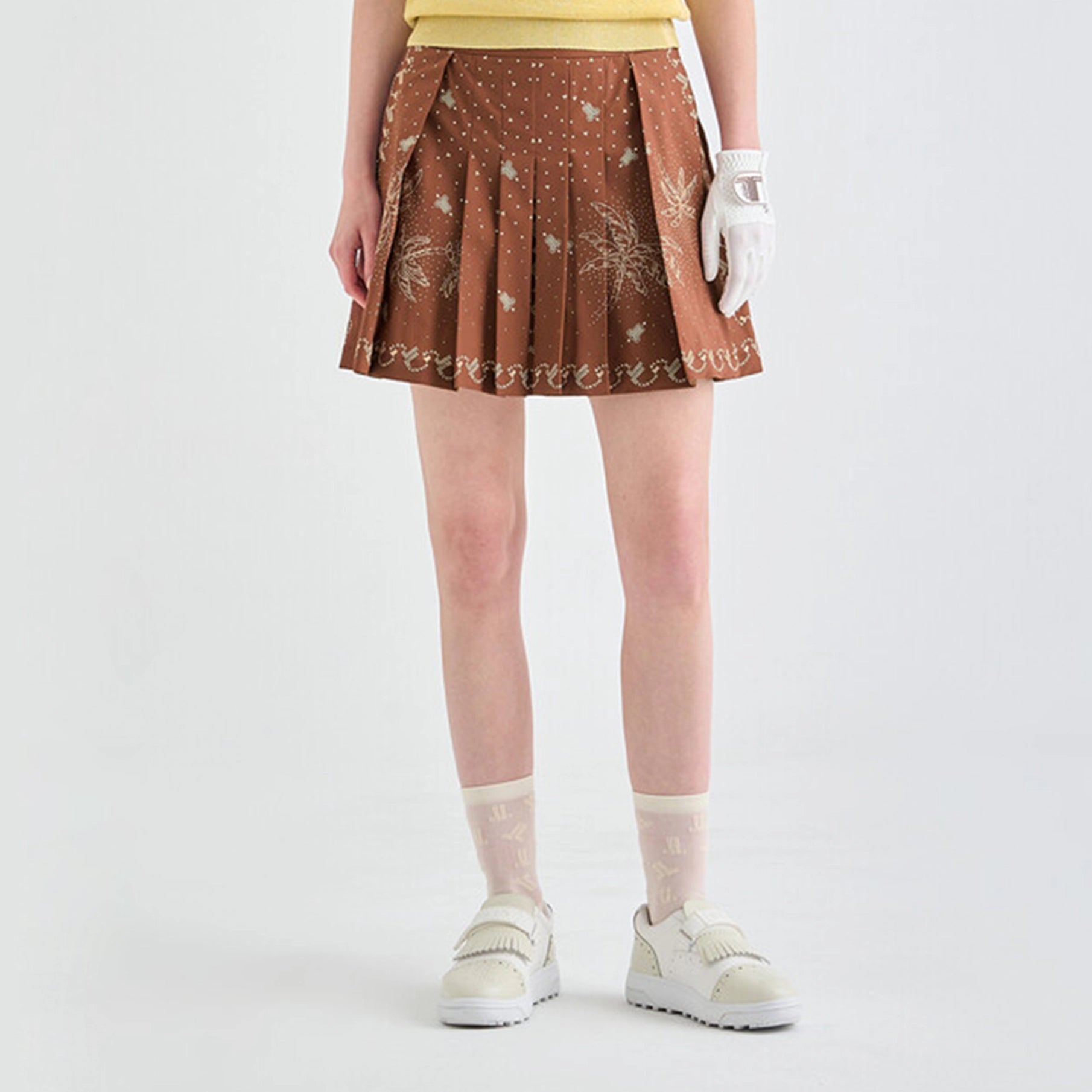 Person wearing a brown pleated skirt with white floral patterns on a light gray background